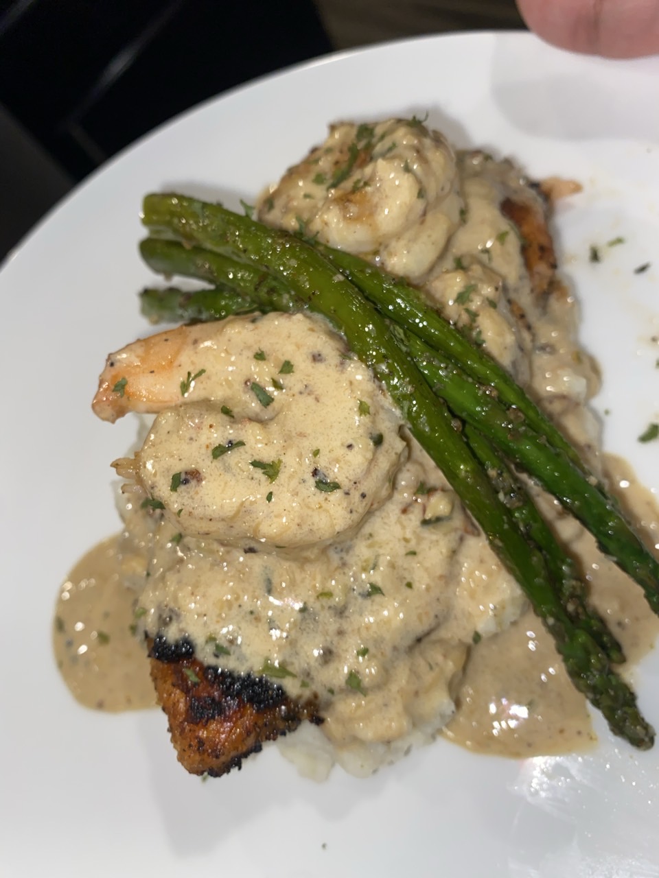 Plate with breaded fish topped with creamy sauce and two green asparagus spears.