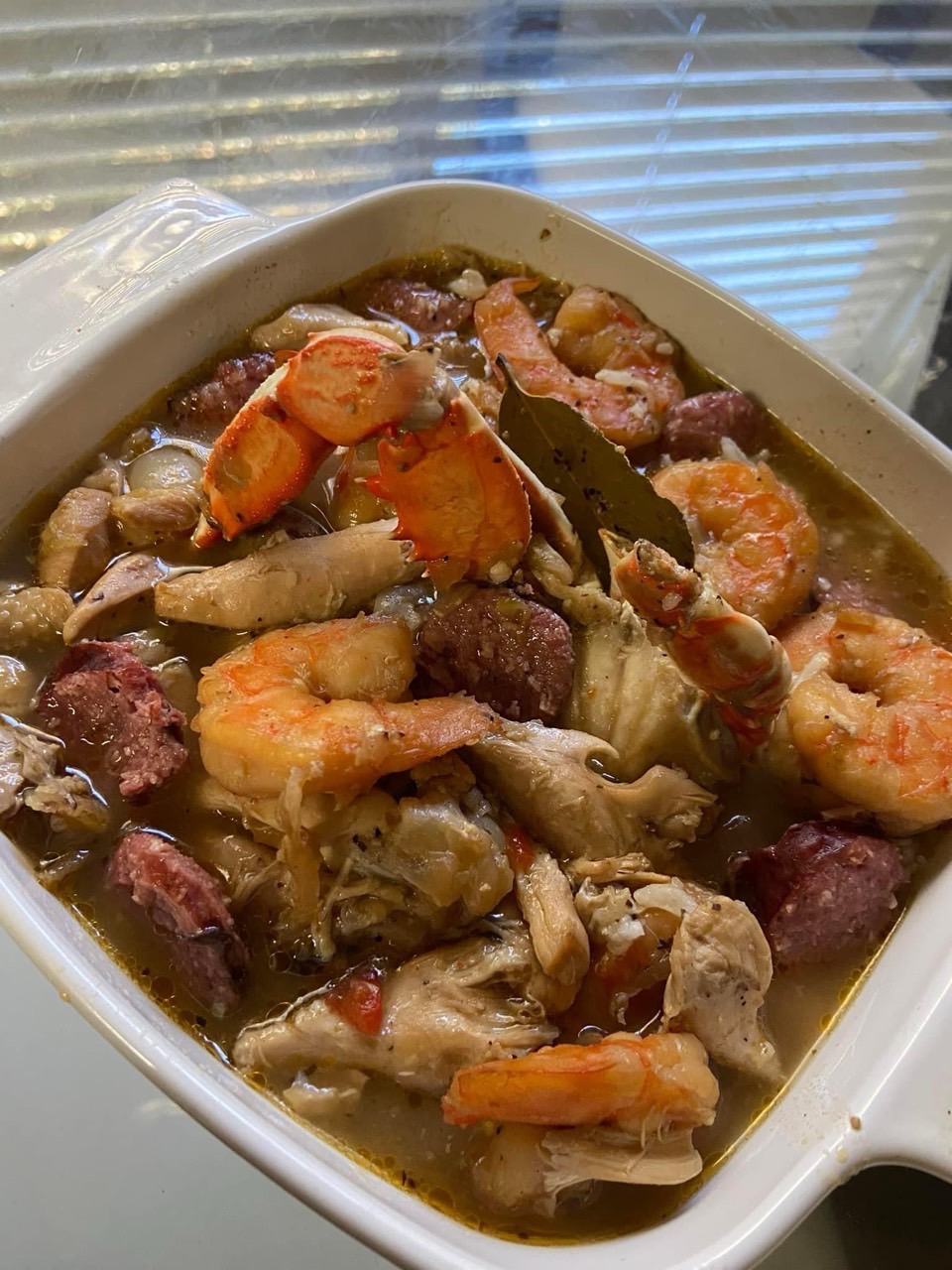 Dish with shrimp, sausage, and vegetables in a bowl, with a spoon partially submerged.