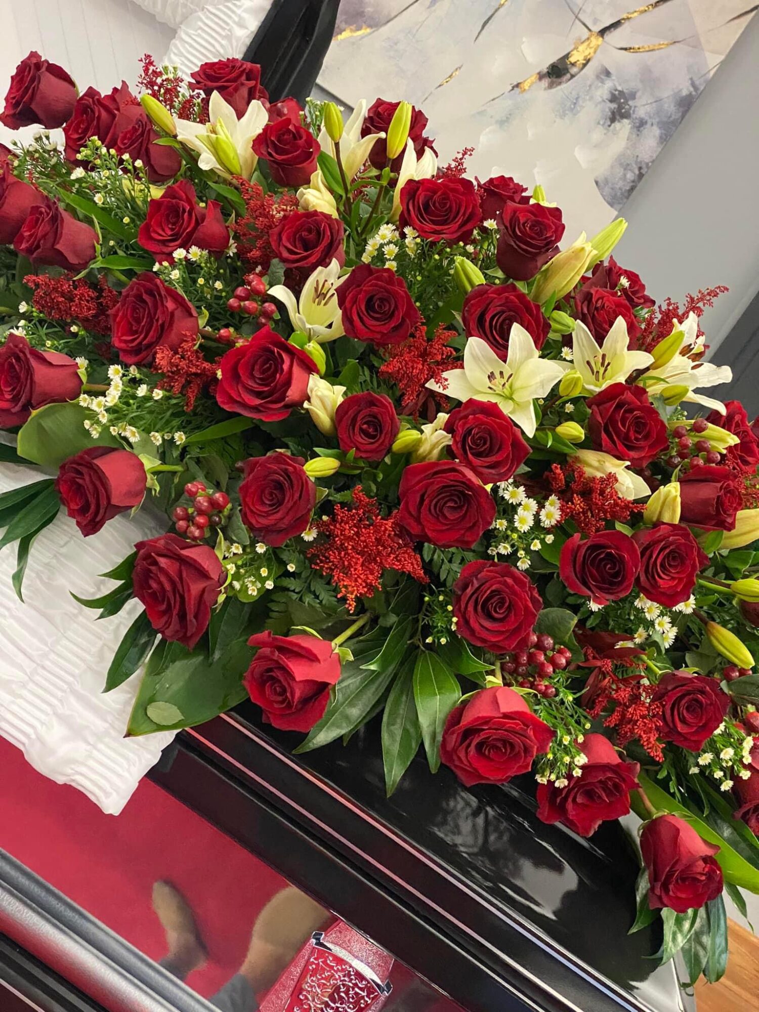Arrangement of red roses, white lilies, and green foliage on a black surface.
