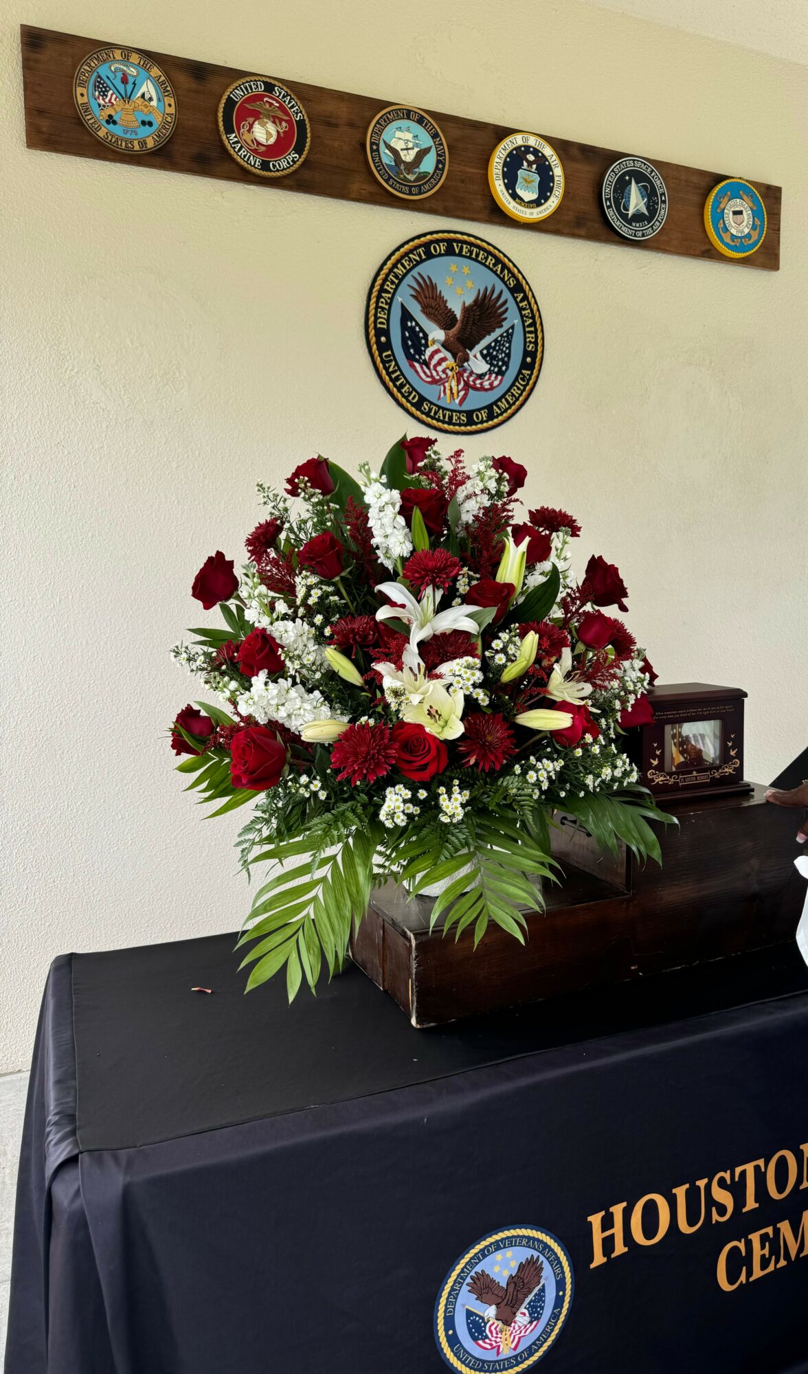 Large floral arrangement with red and white flowers on a table with a black cloth, Houston Cemetery emblem visible.