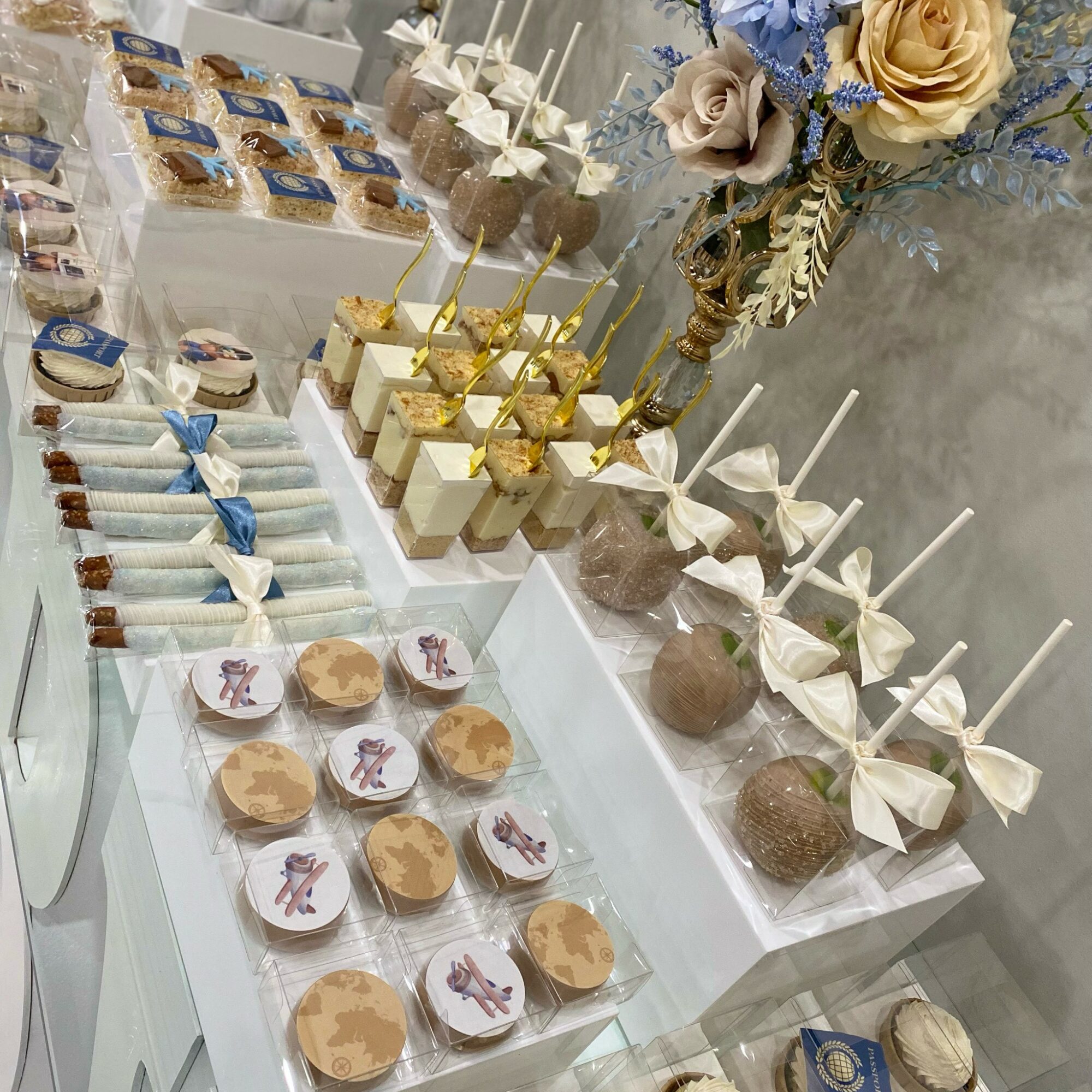 Dessert table with cupcakes, cake pops, and decorated treats, with flowers in the background.