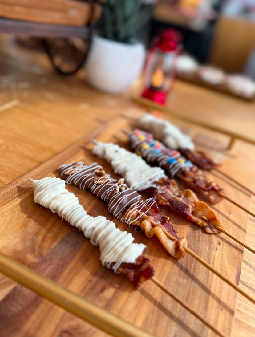 Four skewers with various chocolate-covered and decorated treats on a wooden surface.