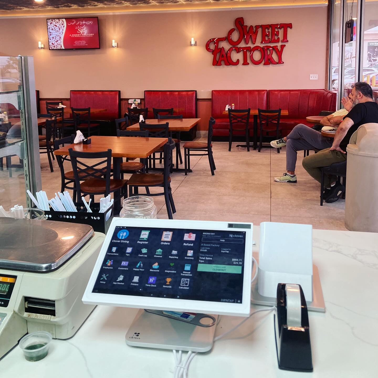 Counter with a tablet, printer, and tape dispenser in a cafe, with seating and a person in the background.