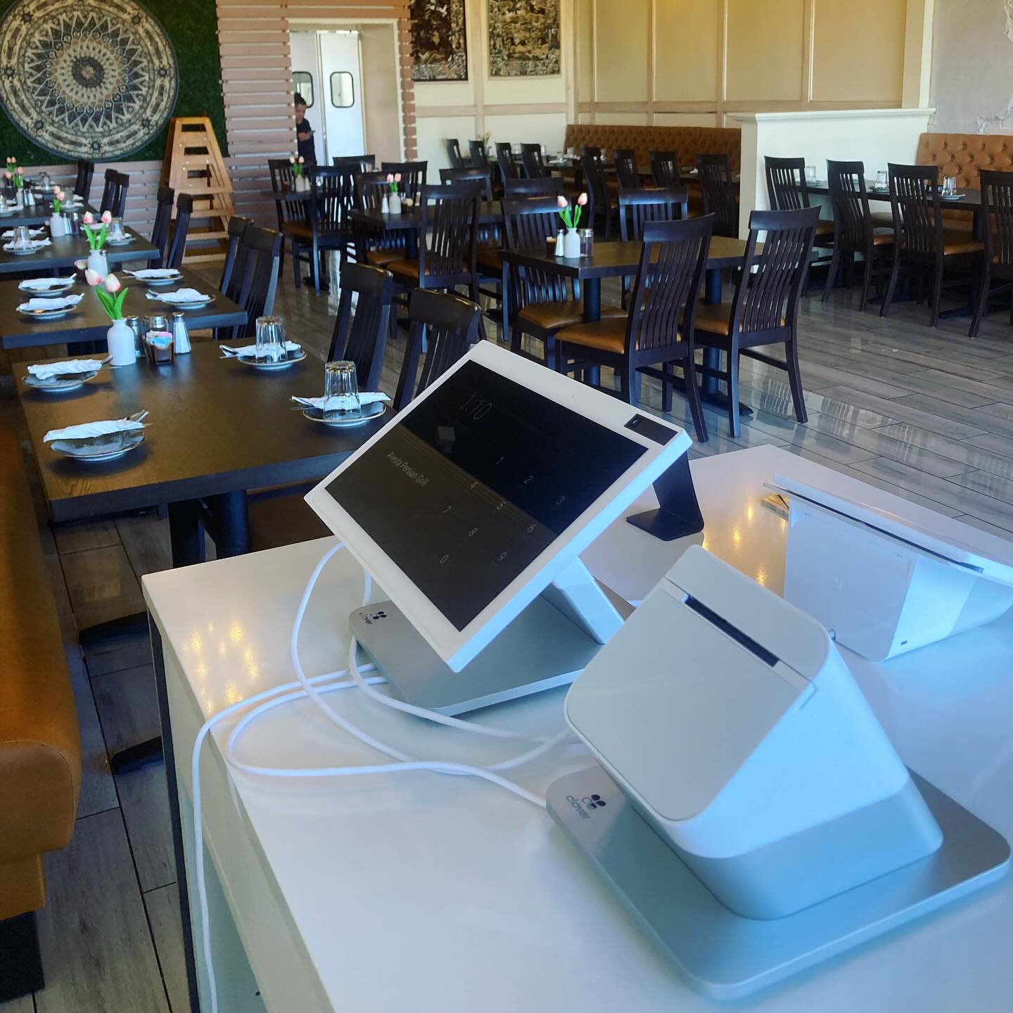 Point-of-sale device with a touchscreen monitor and receipt printer on a white table in a restaurant.