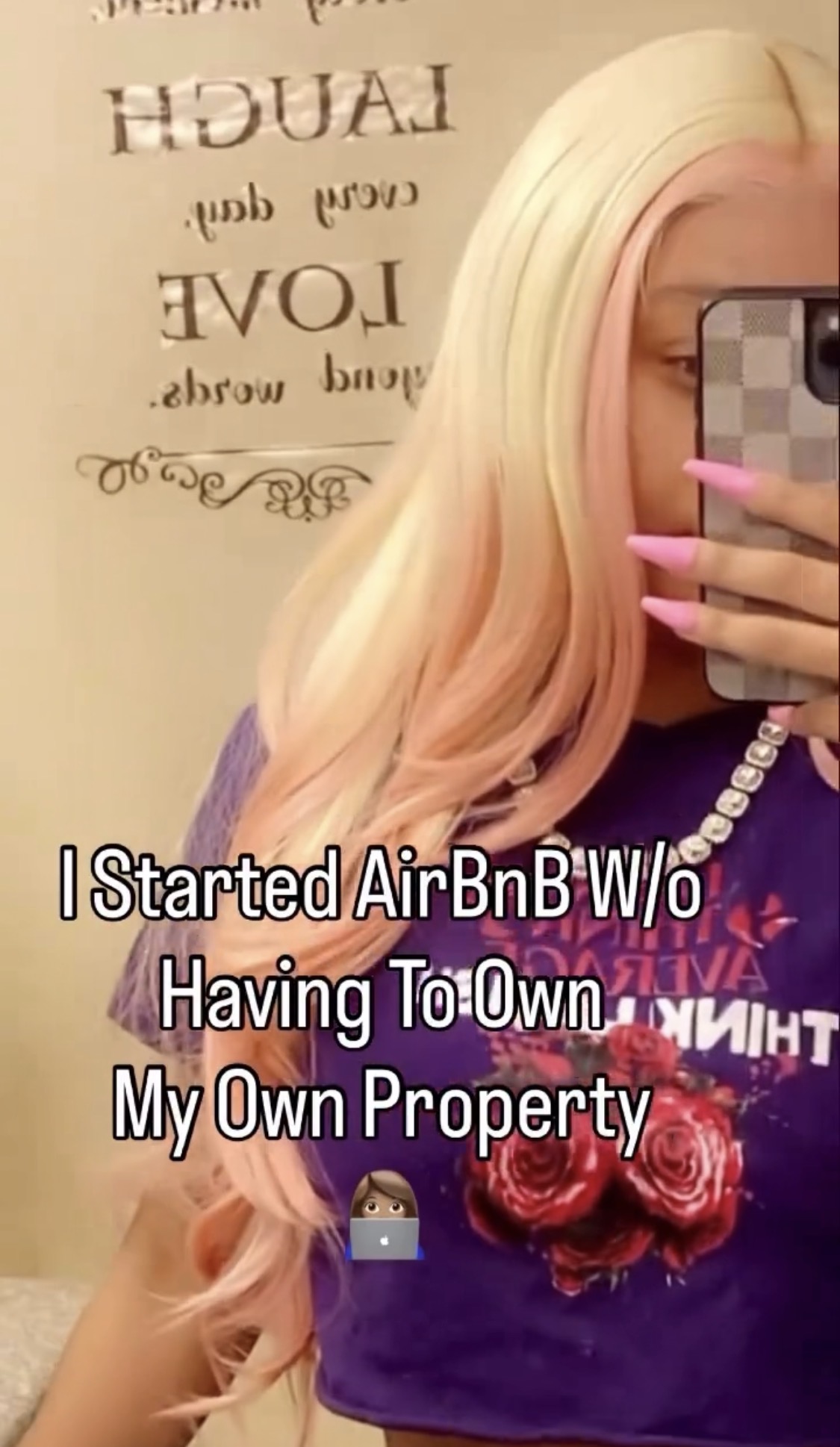 Person with long blonde hair taking a selfie, covering face, wearing a purple top with floral design, holding phone.