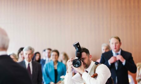 Photographer taking a picture at a formal event with guests seated at tables in the background.