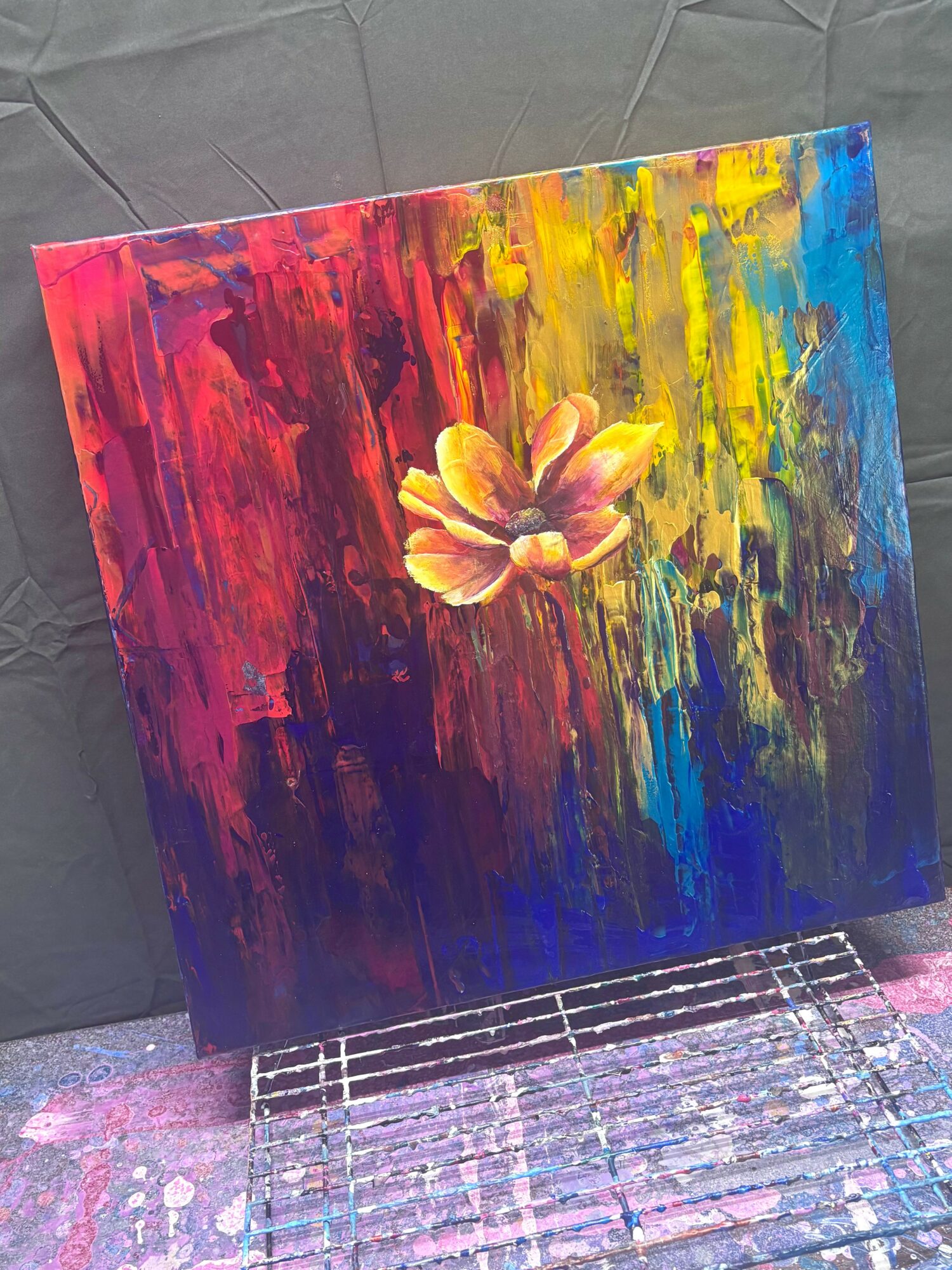 Abstract painting with a central flower, vibrant colors including red, yellow, blue, and purple, on a textured canvas.