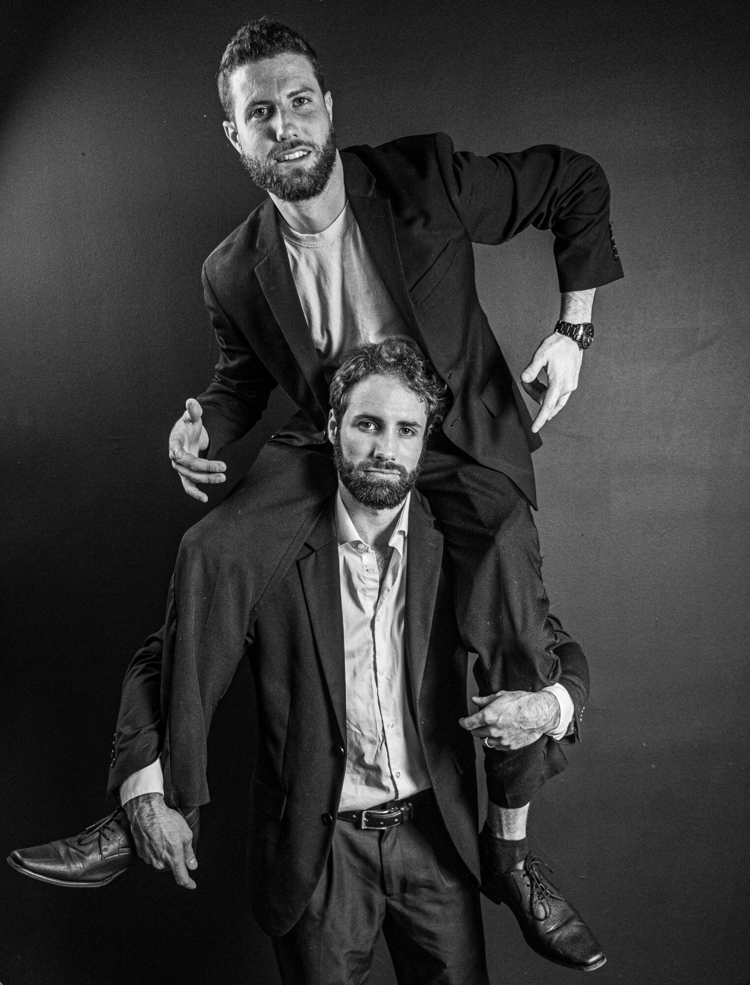 Two men in suits, one standing and one sitting, against a plain background.