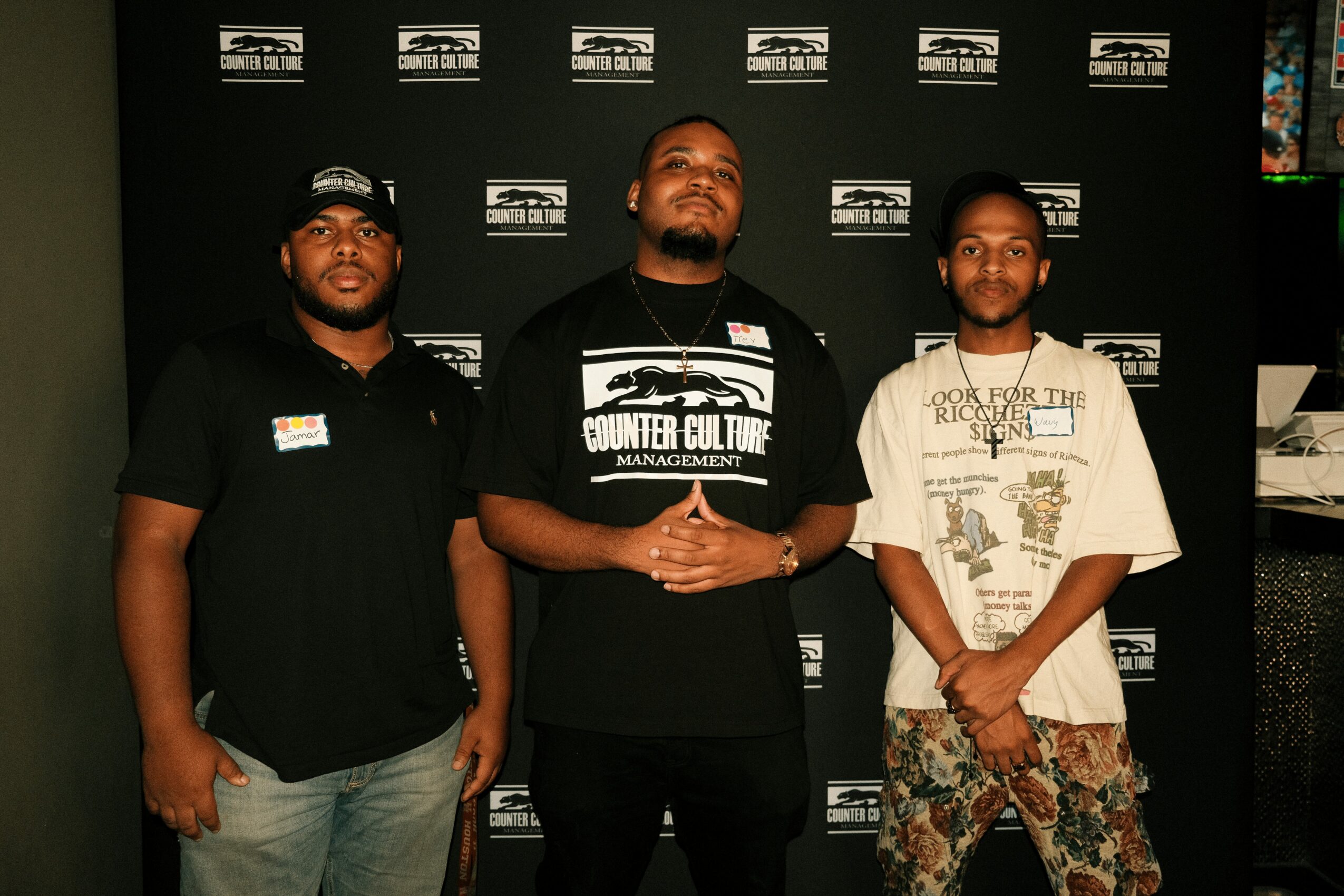 Three men standing in front of a black backdrop with logos, posing for a photo.