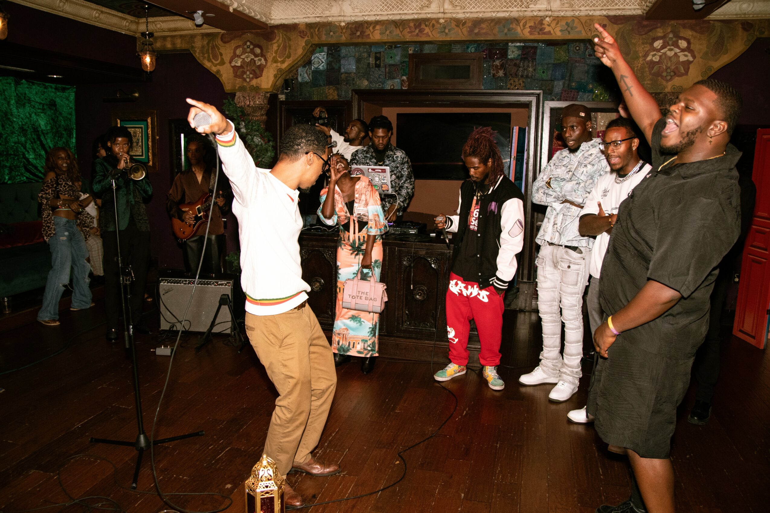 Group of people dancing and socializing in a dimly lit indoor venue with wooden floors and decorative ceiling.