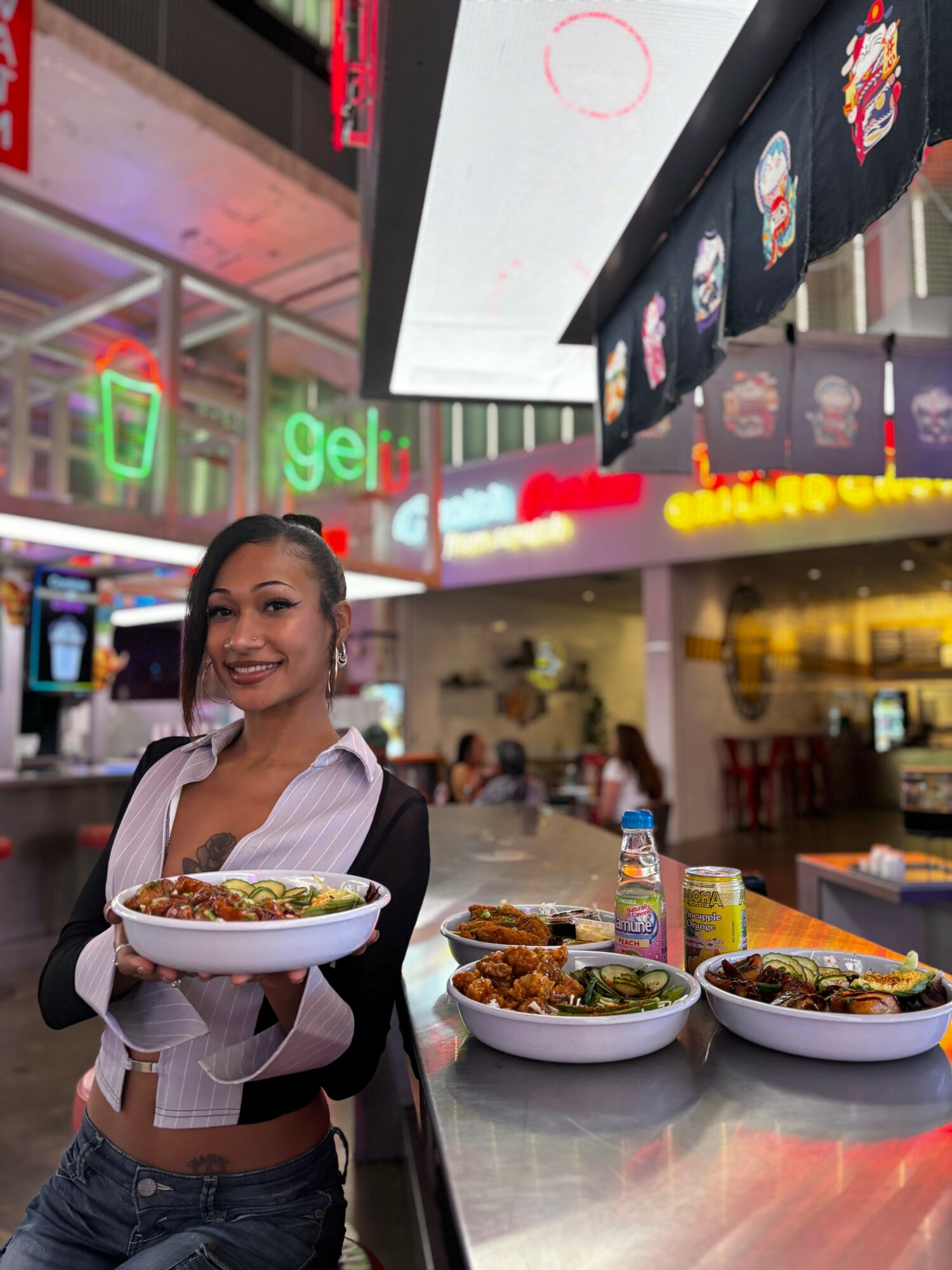 Smiling woman holding a bowl of food in a restaurant or food court setting.