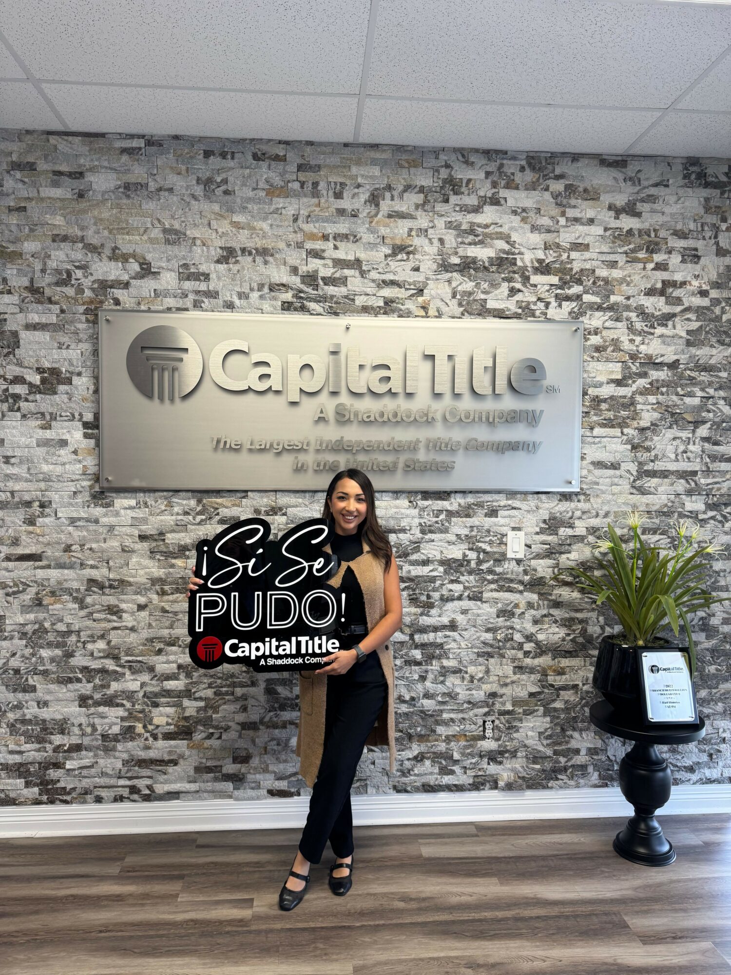 Woman holding a sign in front of a textured wall with a sign reading 'Capital Title'.
