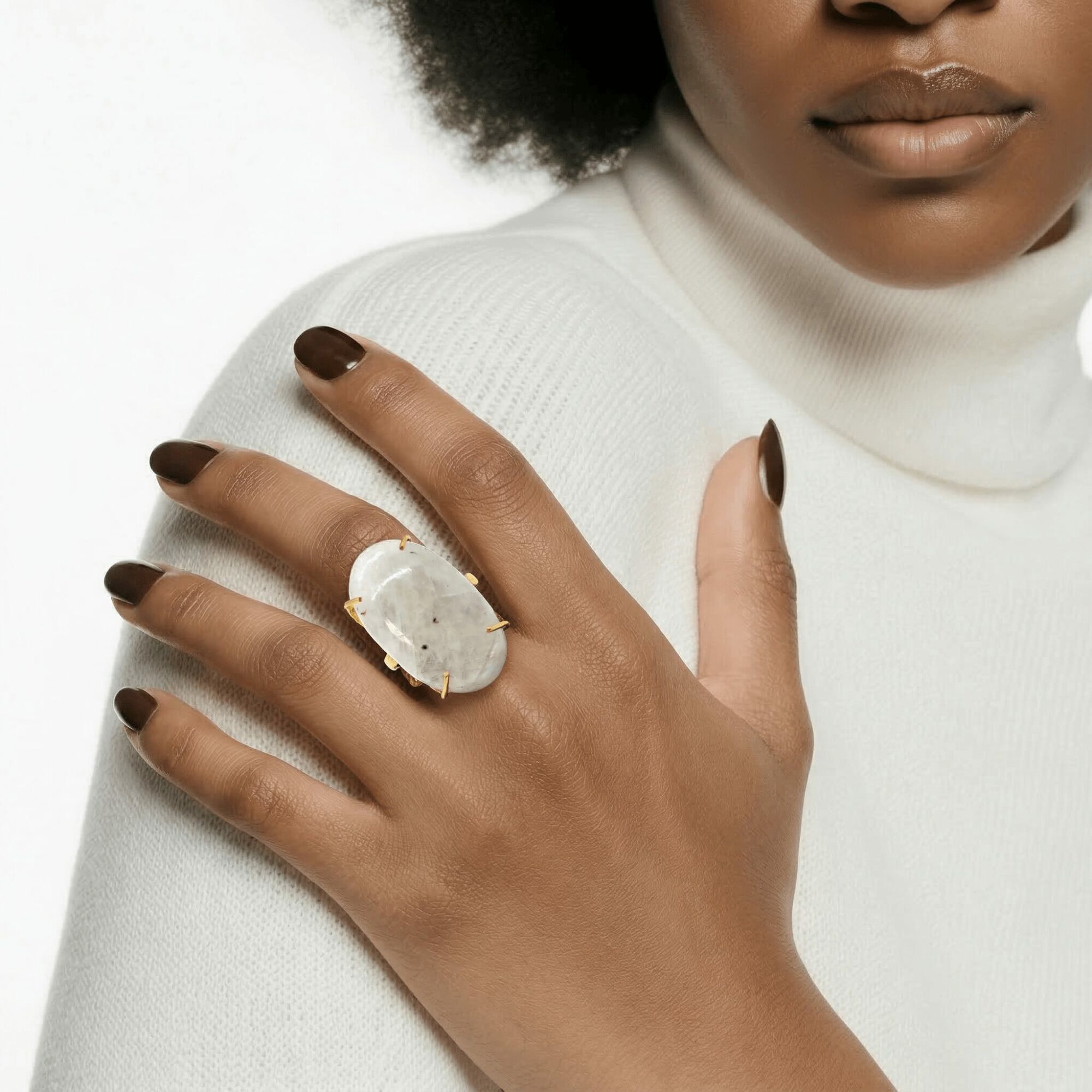 Close-up of a woman wearing a white turtleneck, showing her hand with a large oval ring on her finger.