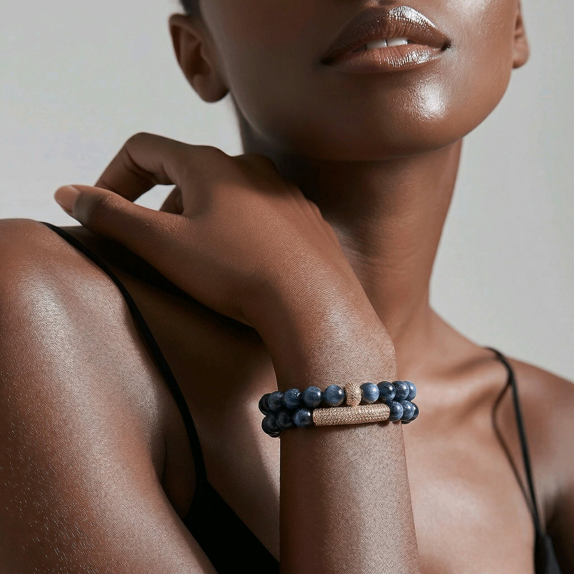 Close-up of a person with dark skin wearing a beaded bracelet on their wrist, with a neutral background.