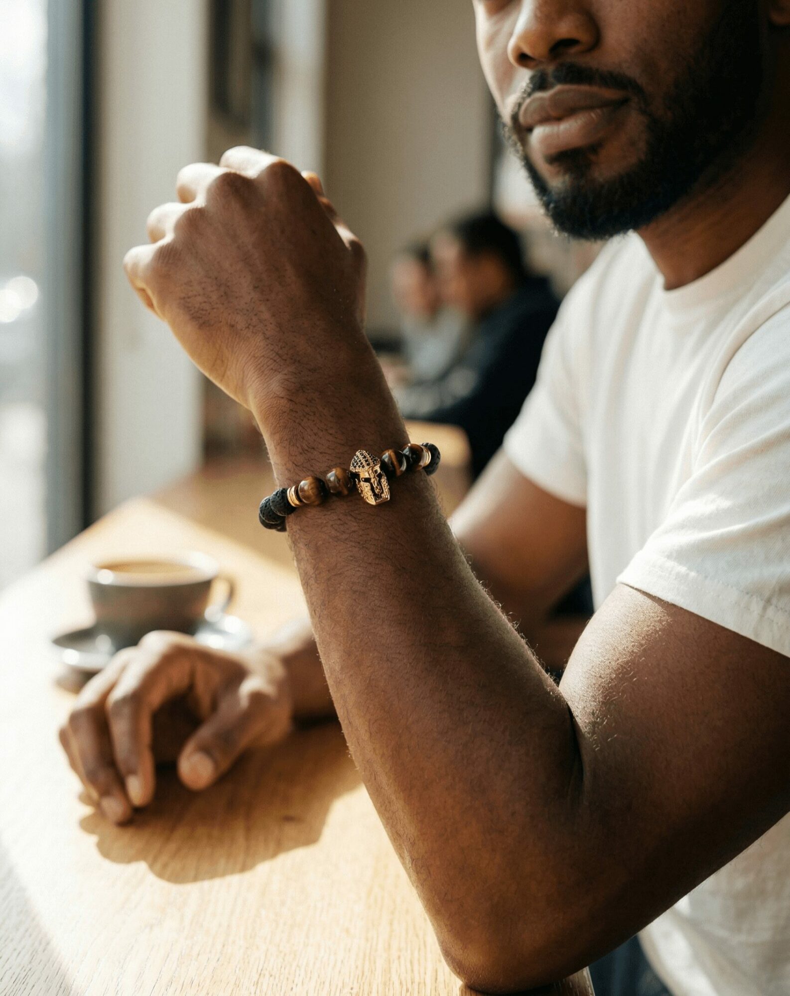 Close-up of a man sitting at a table with a bracelet on his wrist, holding his fist near his face.