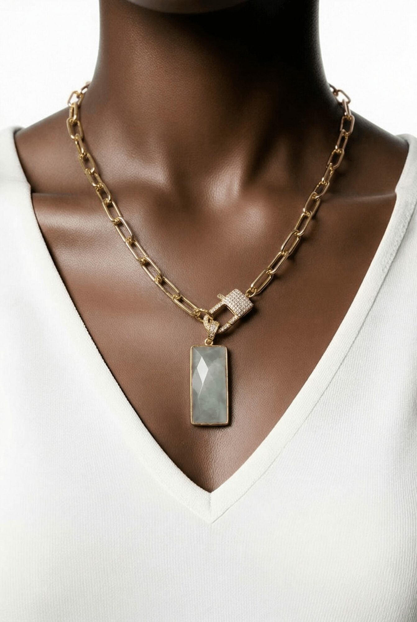 Close-up of a person wearing a gold chain necklace with a rectangular pendant, against a white top.
