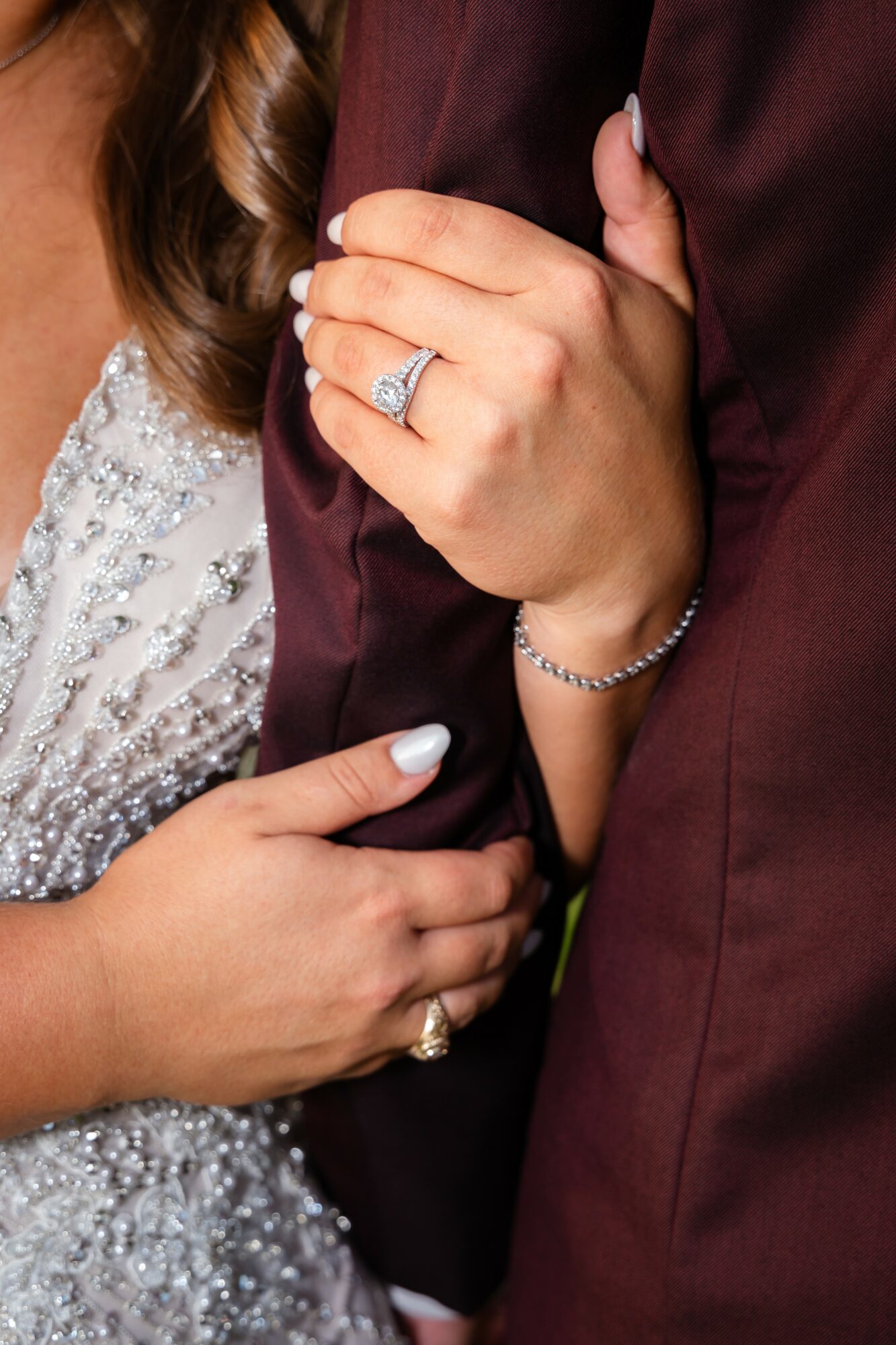 Close-up of a woman’s hand with an engagement ring resting on a man's arm, both dressed formally.