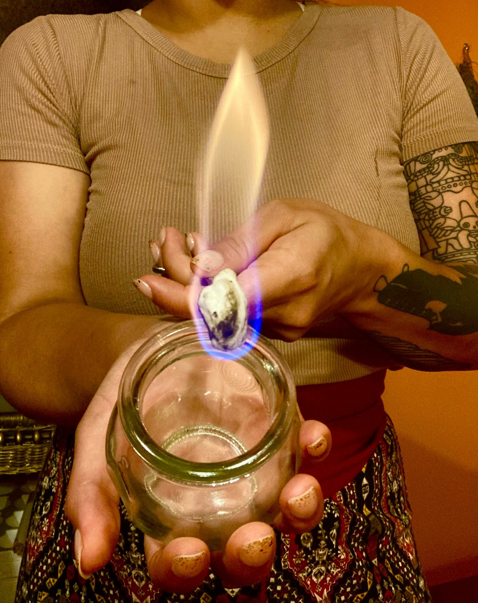 Person holding a glass jar with a lit candle flame above it, in a room with warm lighting.