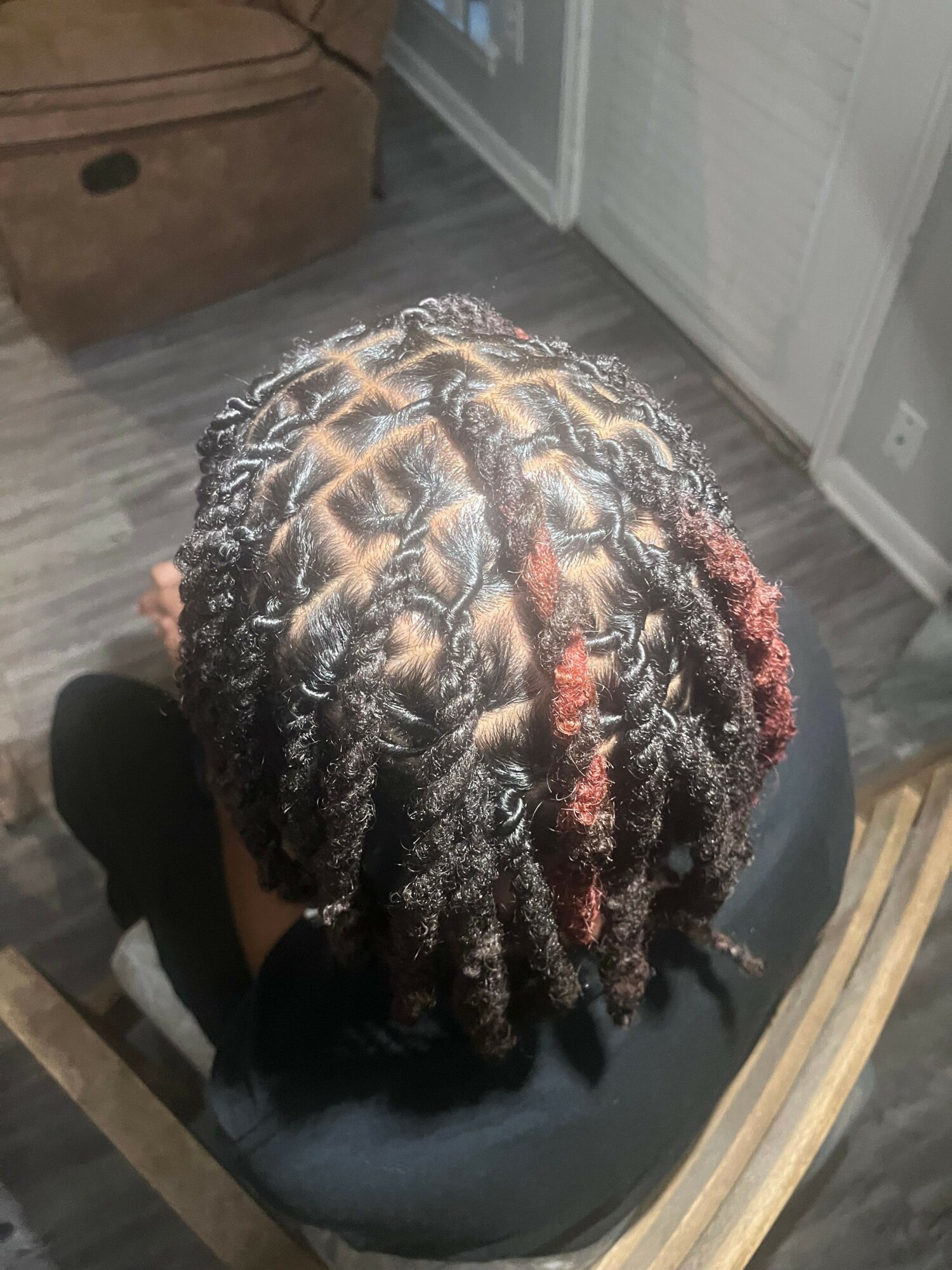 Top view of person with styled, textured dreadlocks with some reddish highlights, sitting on a chair indoors.
