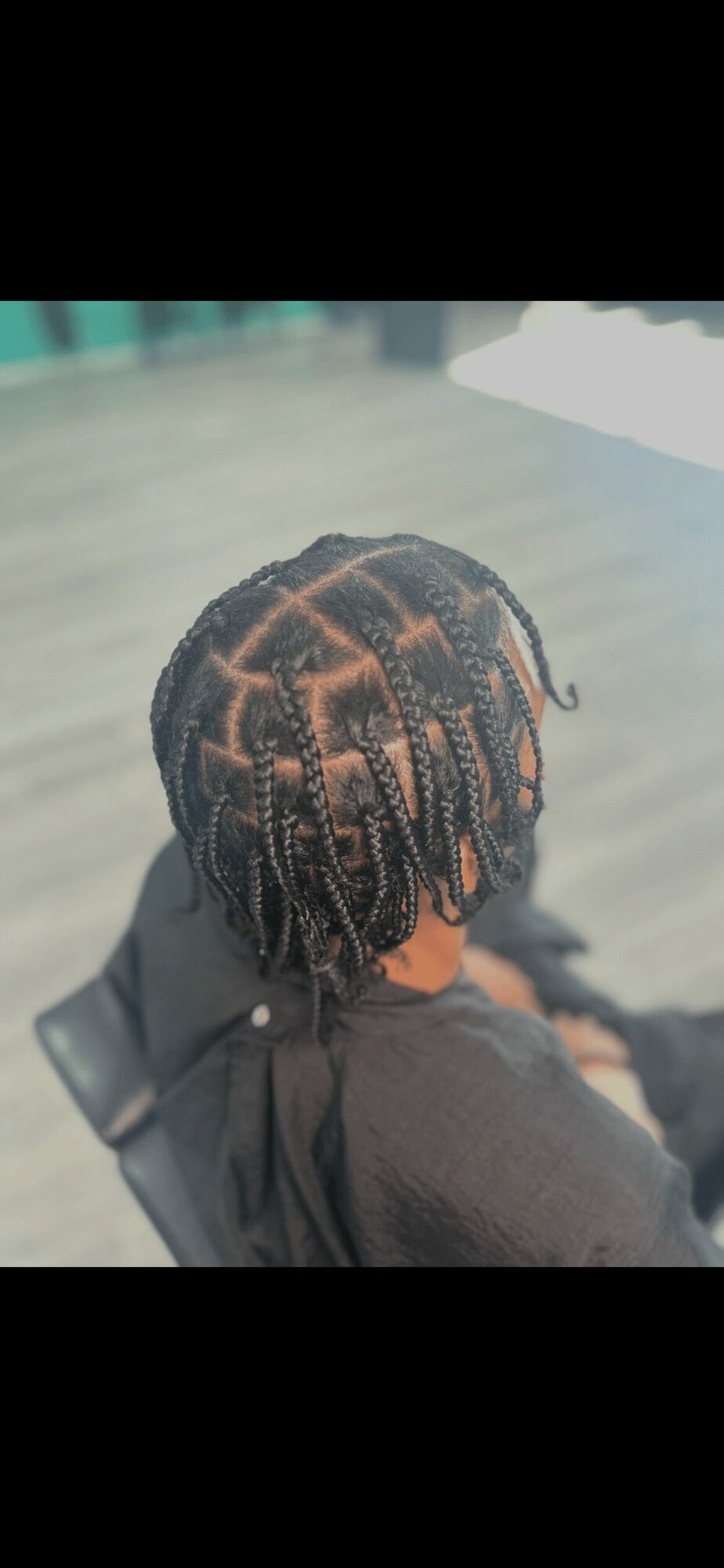 Person with braided hairstyle sitting outdoors on a chair, facing away from the camera.