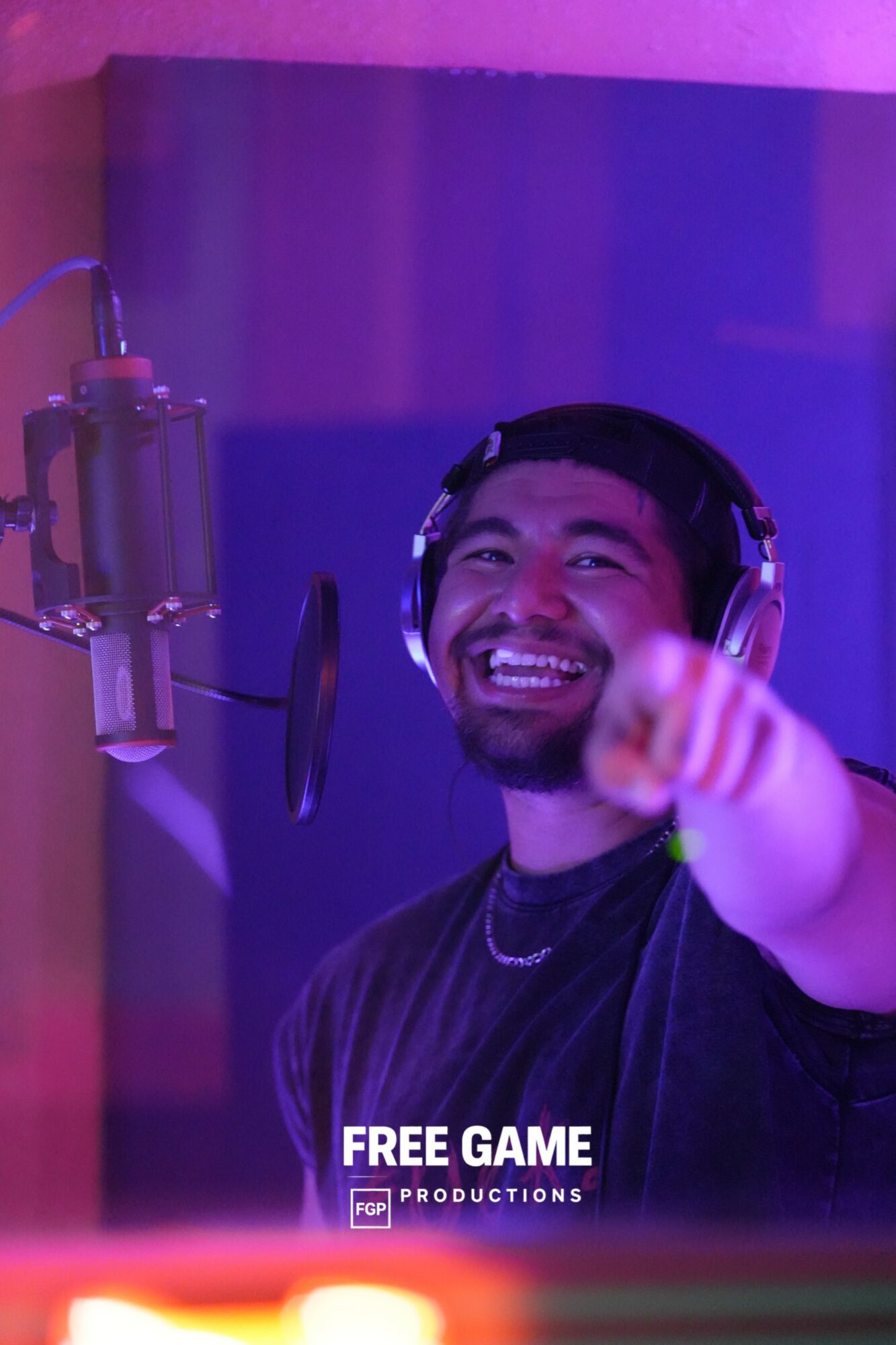 Man in headphones smiling and pointing, recording in a studio with purple lighting.