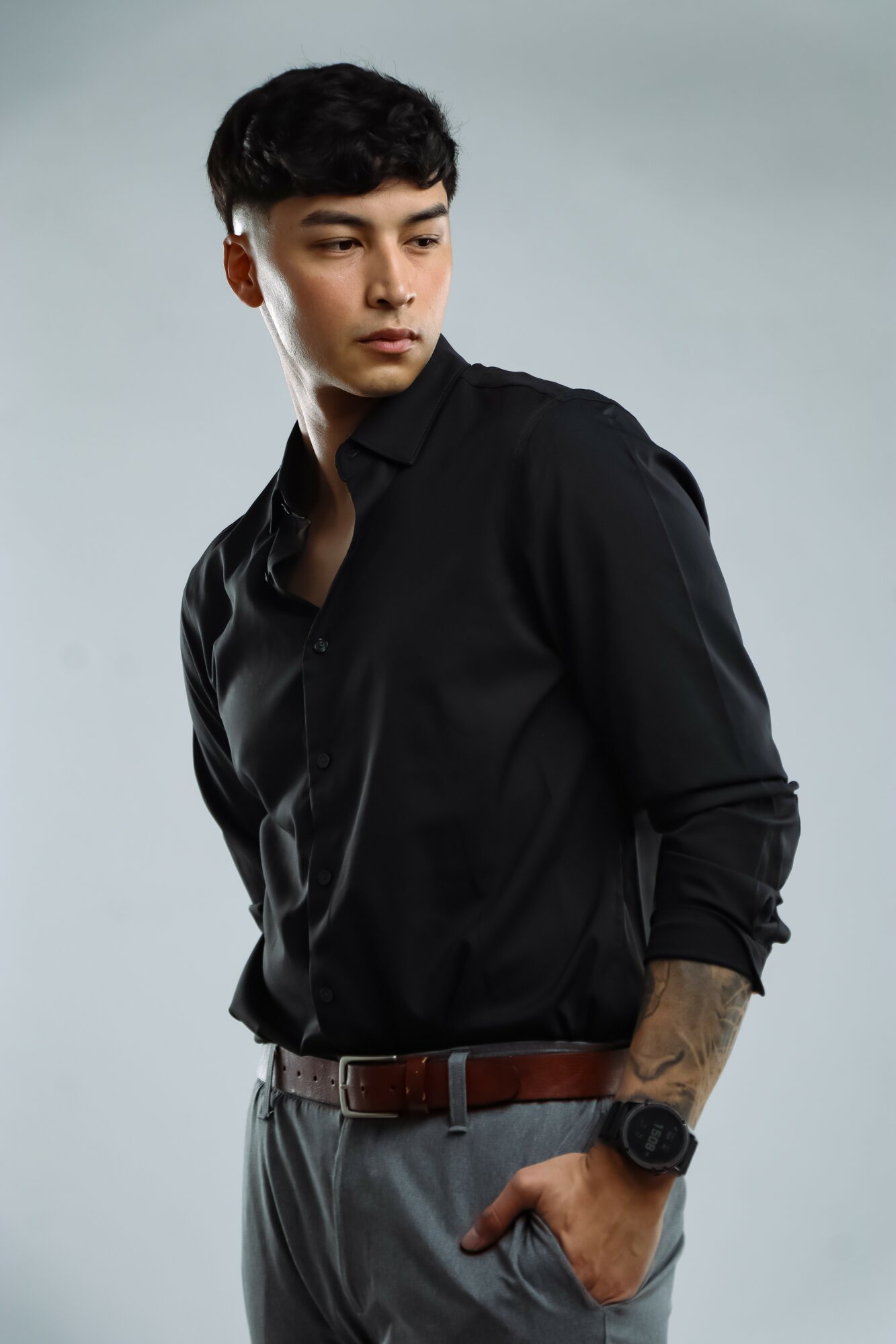 Young man with short dark hair wearing a black shirt and gray pants, standing against a plain background.