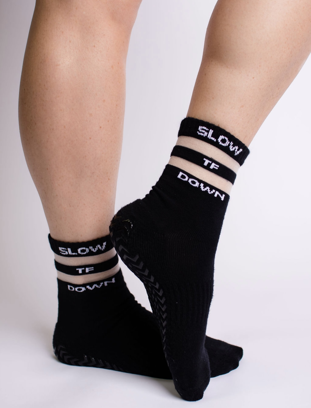 Two legs wearing black socks with white and beige stripes and text, standing on a white background.