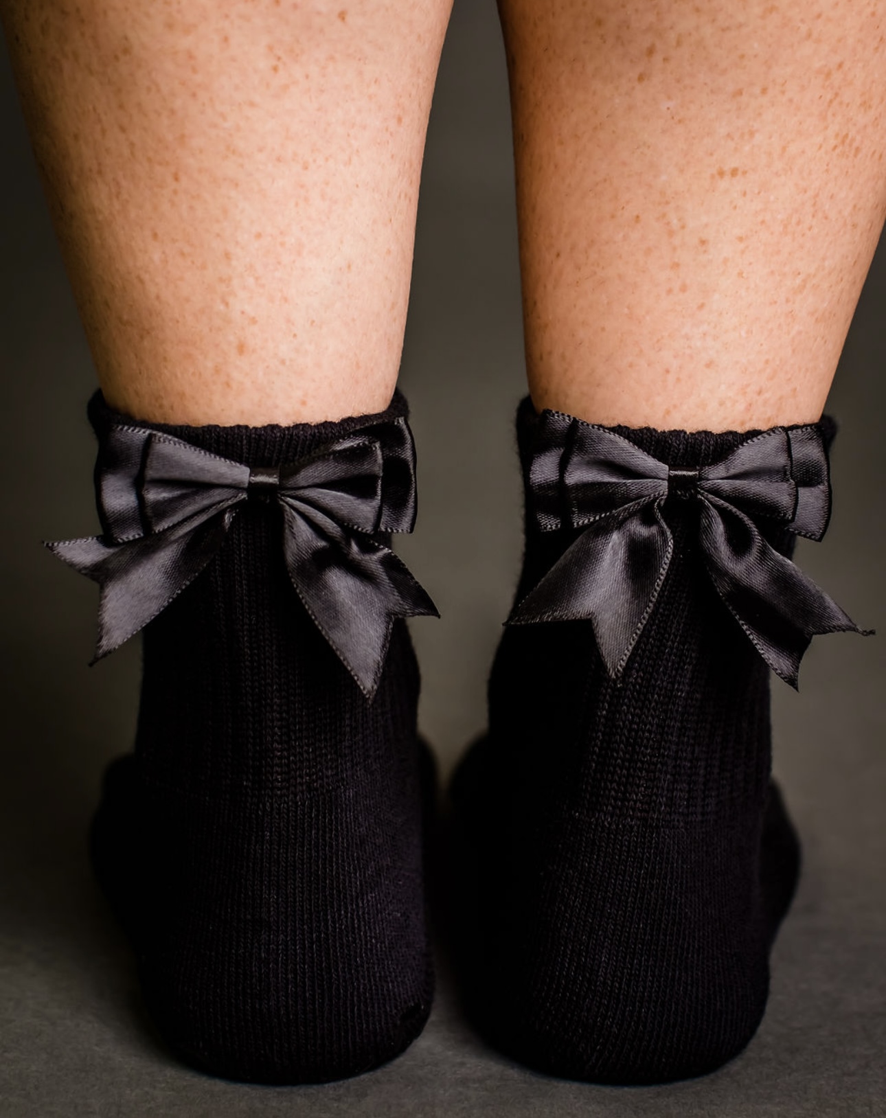 Person wearing black socks with large satin bows, standing with legs apart.