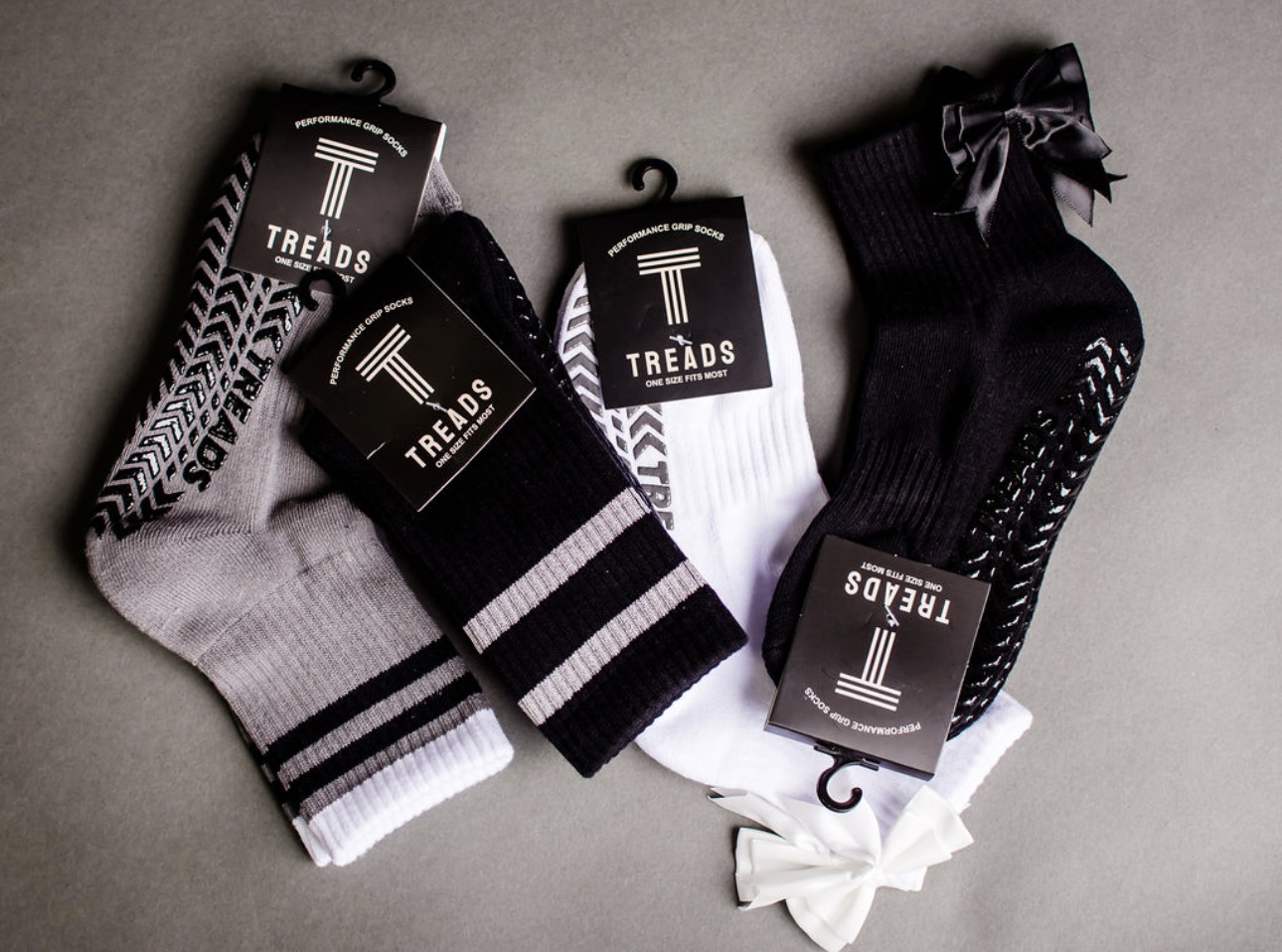Four pairs of socks with different black, white, and gray patterns, some with bows and tags, arranged on a gray surface.