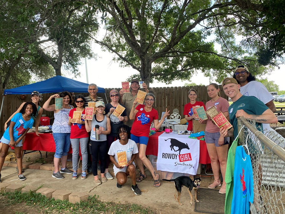 Group of people outdoors holding snacks and a banner, with trees and a fence in the background.