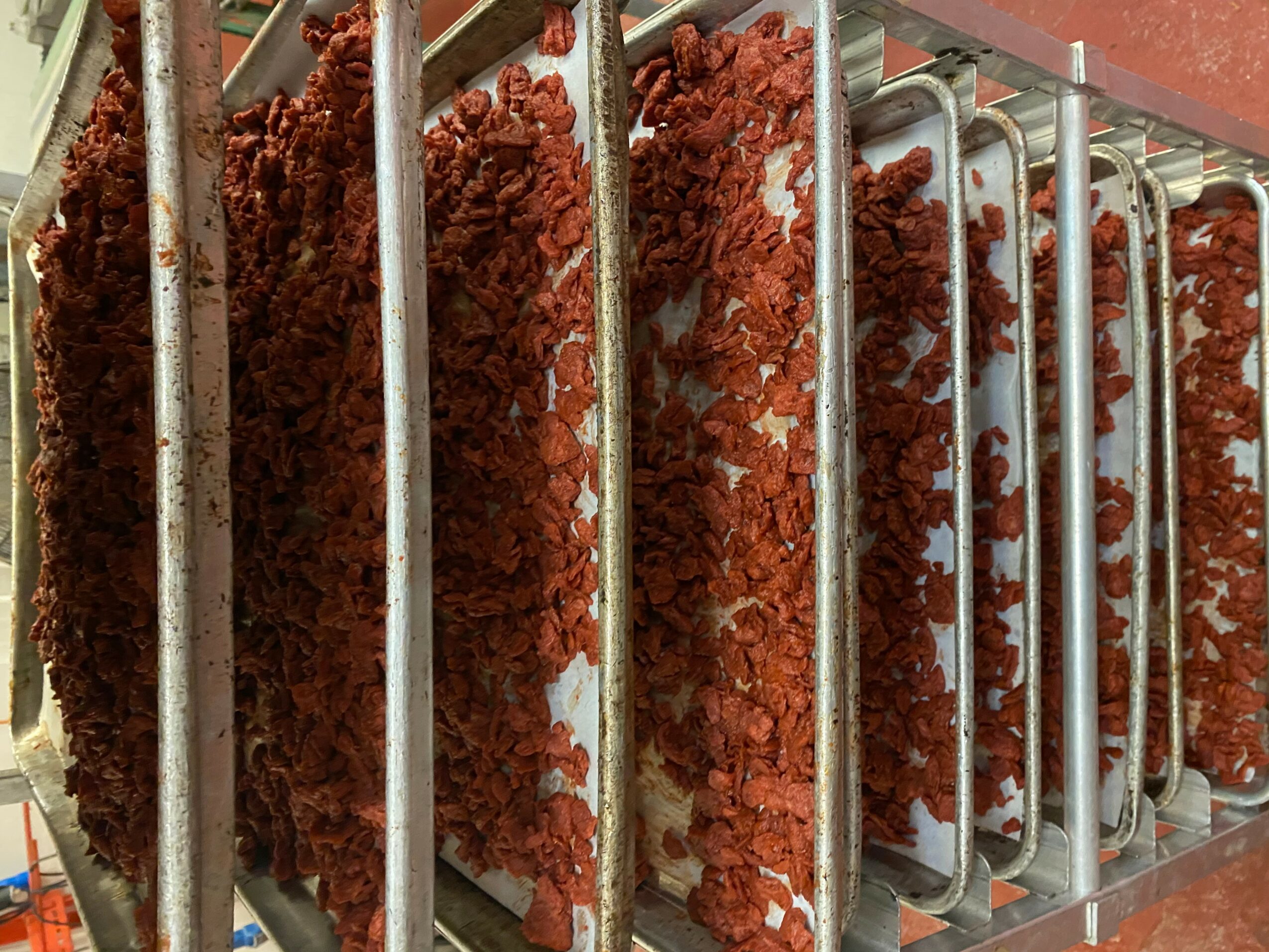 Multiple slices of red meat behind metal bars in a display case.