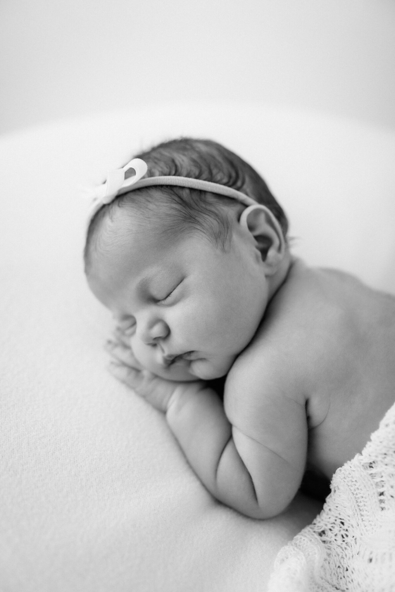 Sleeping newborn baby with head resting on hands, wearing a headband, lying on soft surface.