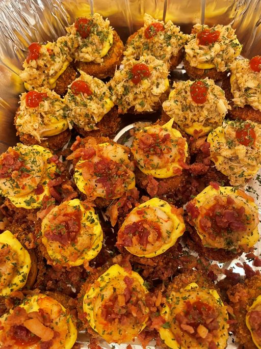 Close-up of fried snacks with breading, topped with red sauce and herbs, arranged on a reflective surface.