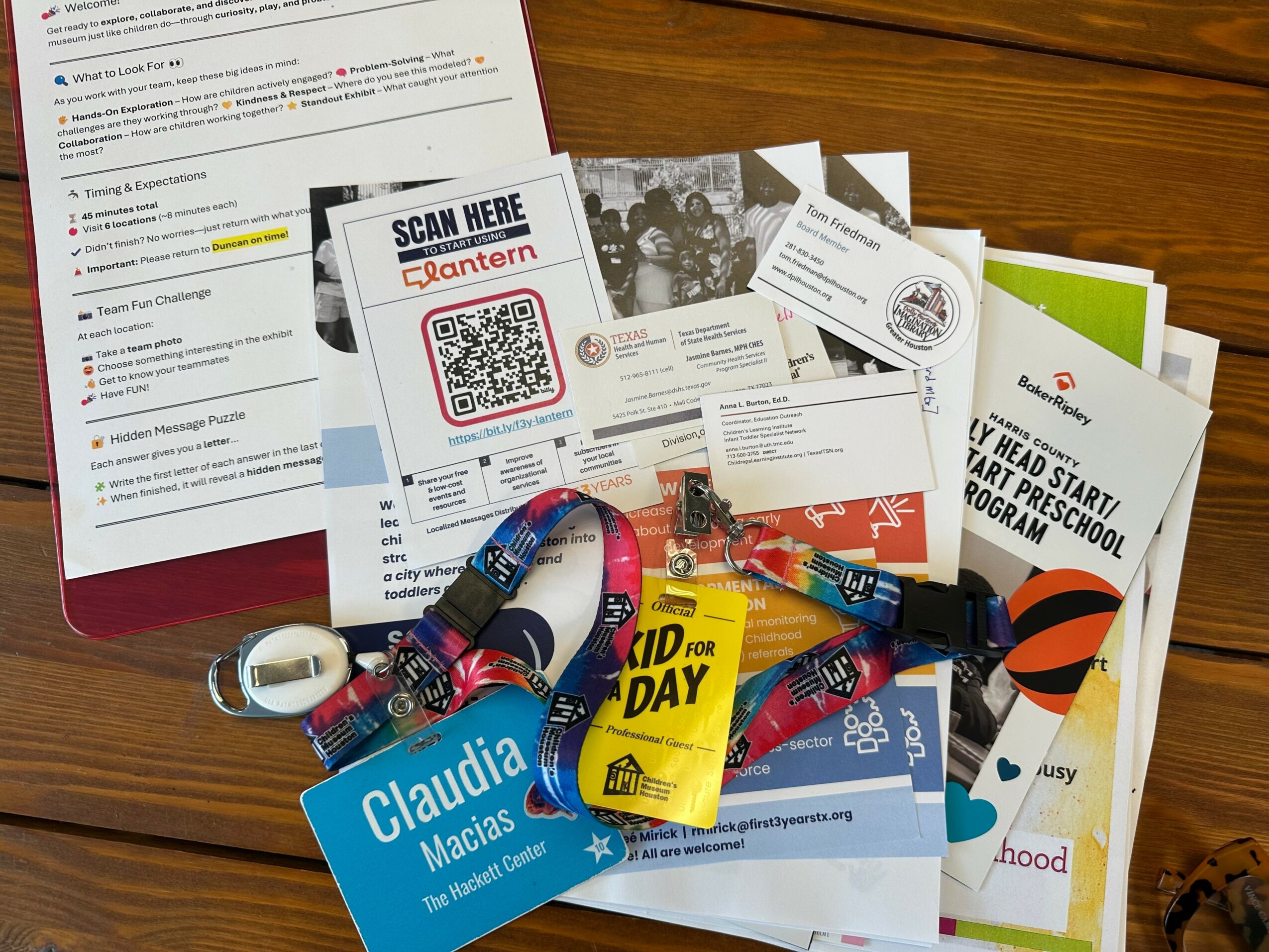 Collection of papers, flyers, and wristbands on a wooden surface, including a QR code and a yellow card.