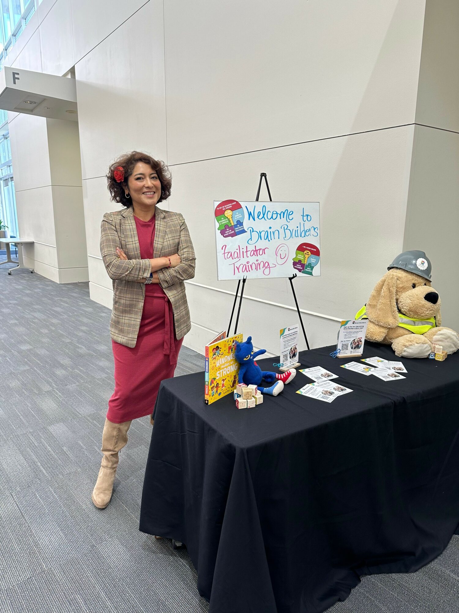 Woman standing next to a table with toys and a colorful welcome sign, in a modern indoor space.