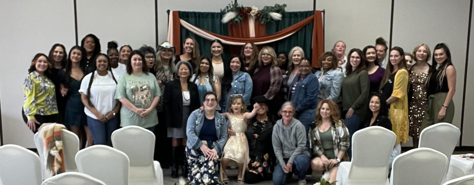 Group of people posing indoors with chairs and decorations in the background.