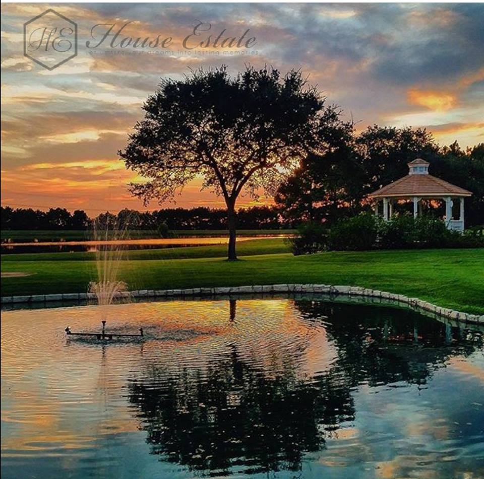 Tree, gazebo, and pond reflecting sunset sky with clouds and colors.