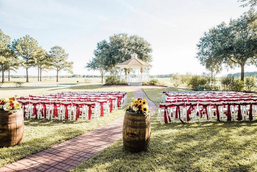 Outdoor wedding setup with rows of chairs, a brick aisle, and a gazebo in the background, surrounded by trees and grass.
