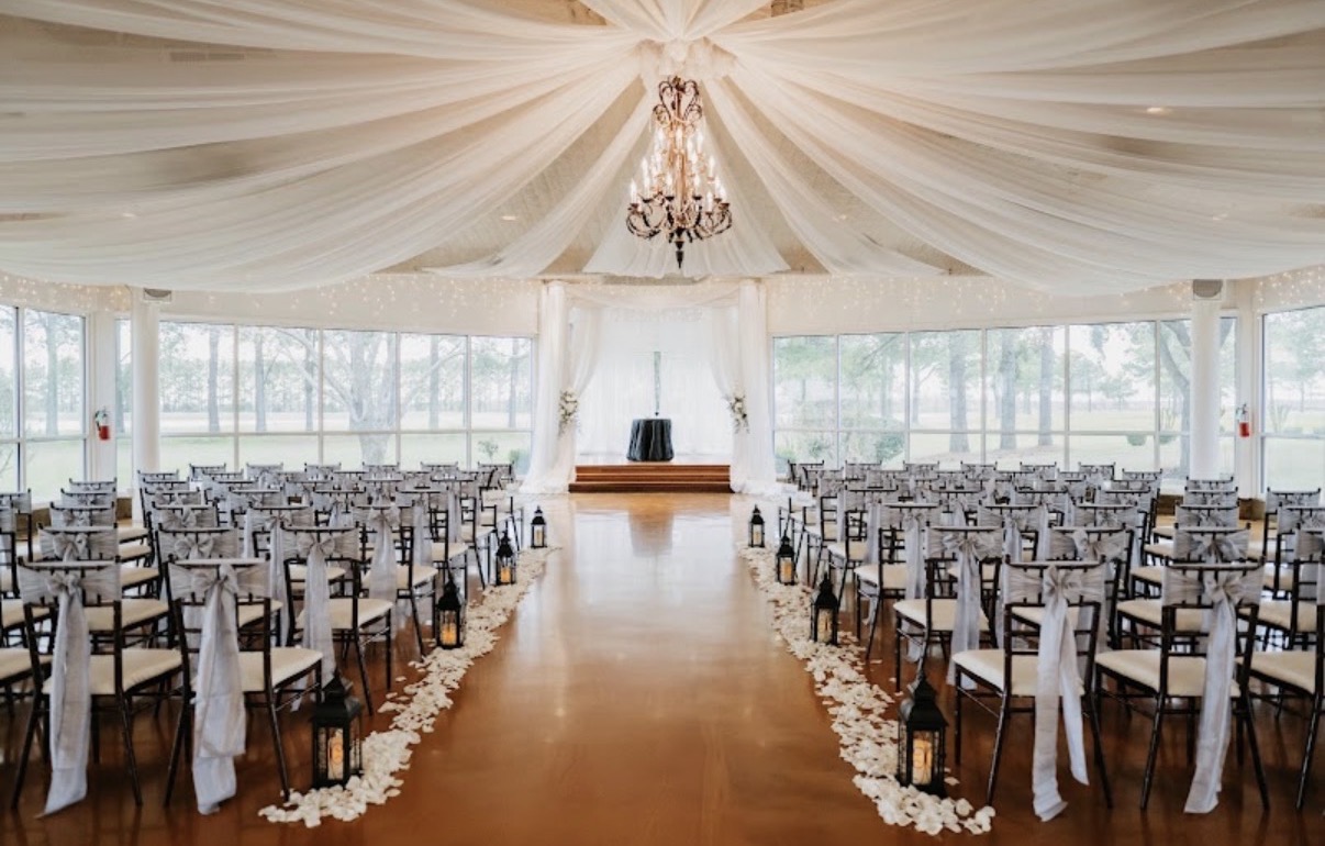 Elegant event hall with rows of chairs, a chandelier, and large windows, decorated for a wedding or celebration.