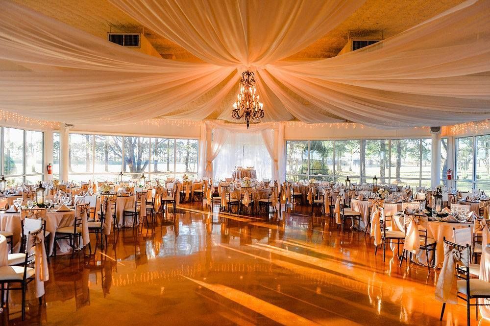 Elegant banquet hall with draped ceiling, chandelier, large windows, and arranged tables with chairs for event.