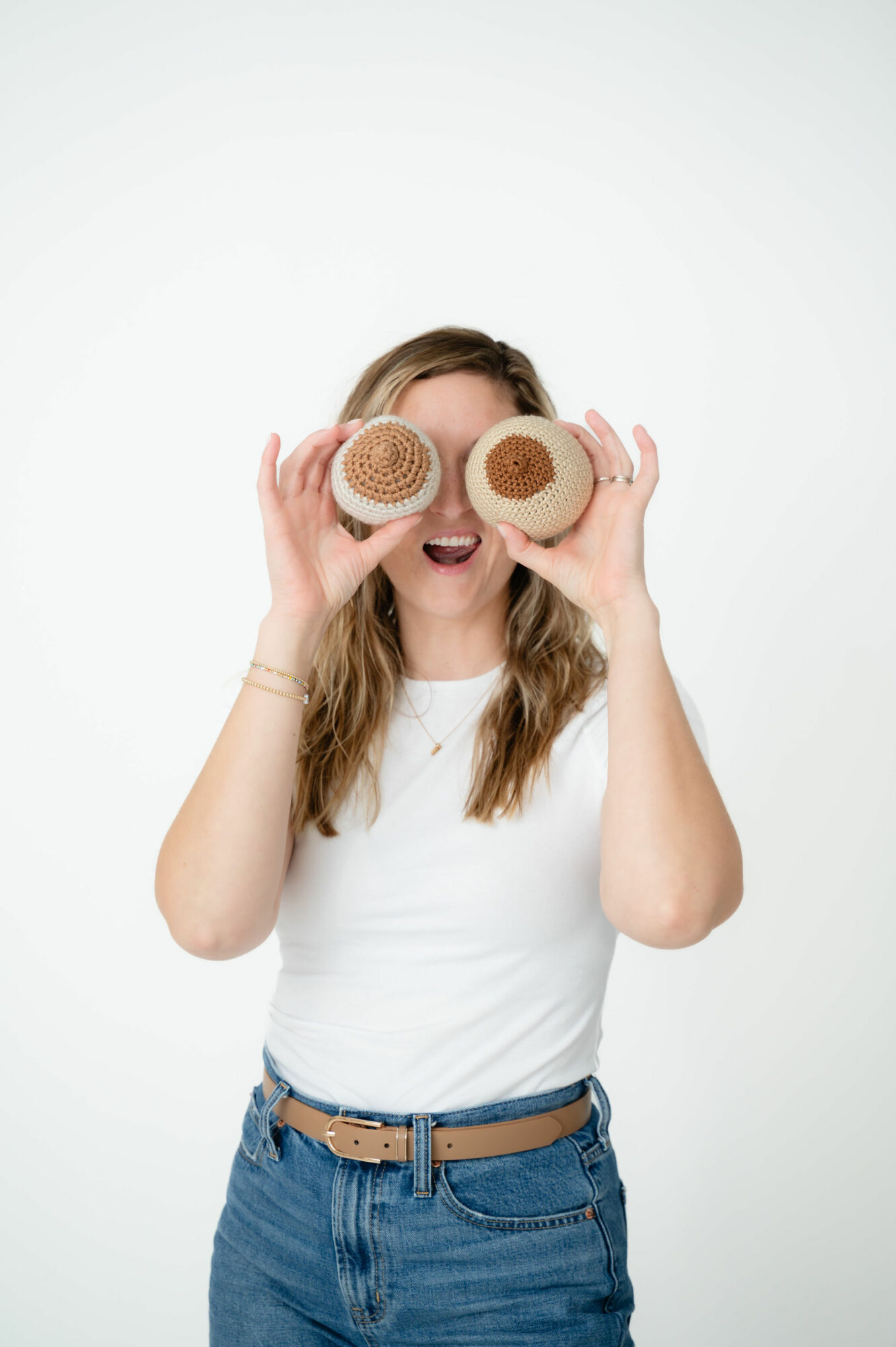 Woman holding two donuts in front of her eyes, smiling, wearing a white shirt and jeans.
