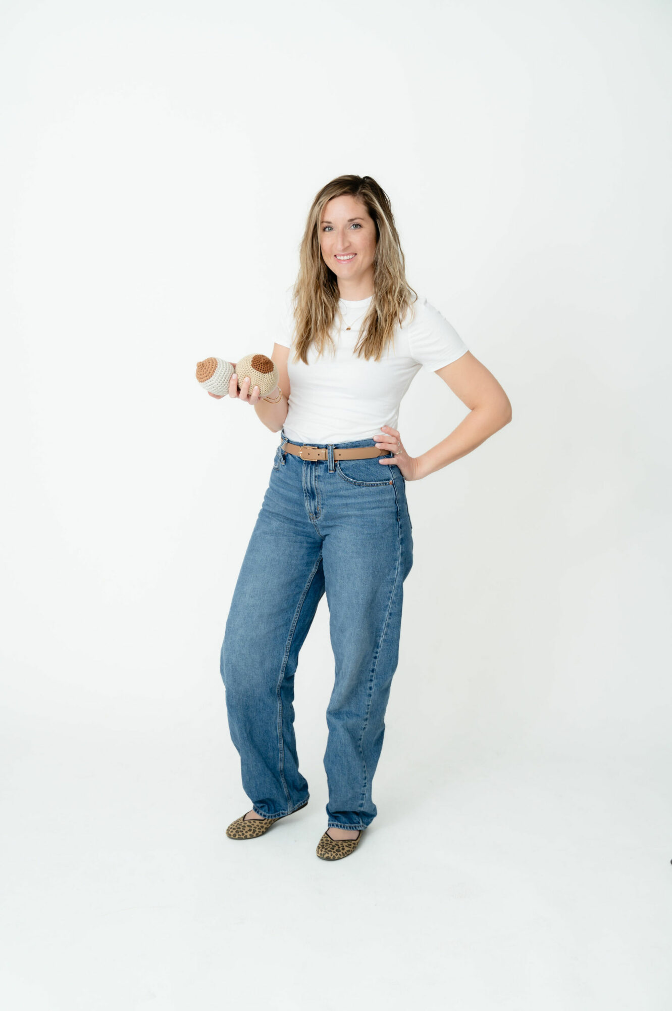 Young woman standing holding a dumbbell, wearing a white t-shirt and blue jeans, smiling.