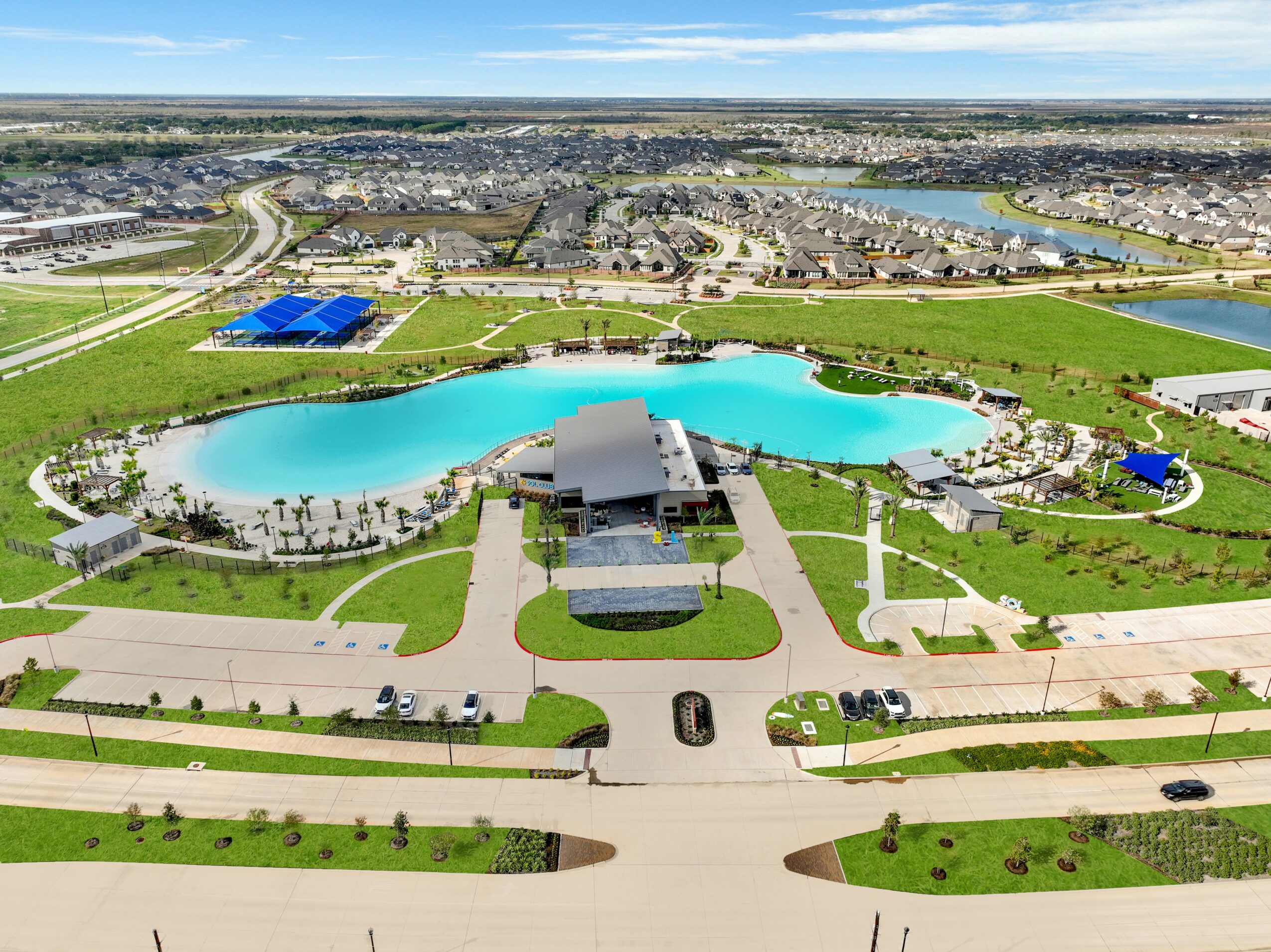 Aerial view of a park with a large irregular-shaped lake, surrounding green lawns, pathways, and a building near the water.