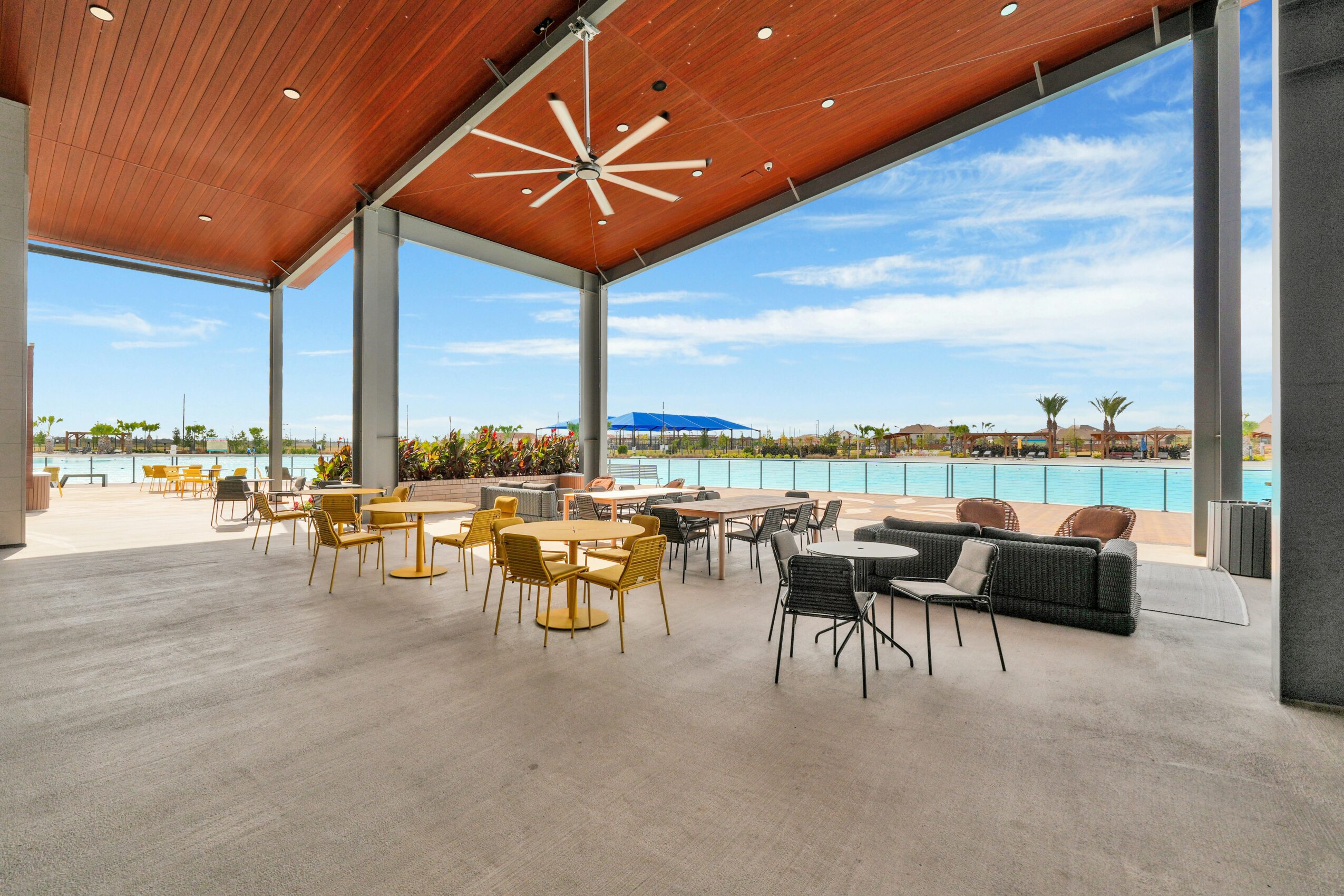Spacious indoor area with large glass windows, wooden ceiling, modern furniture, and a view of a pool and outdoor landscape.