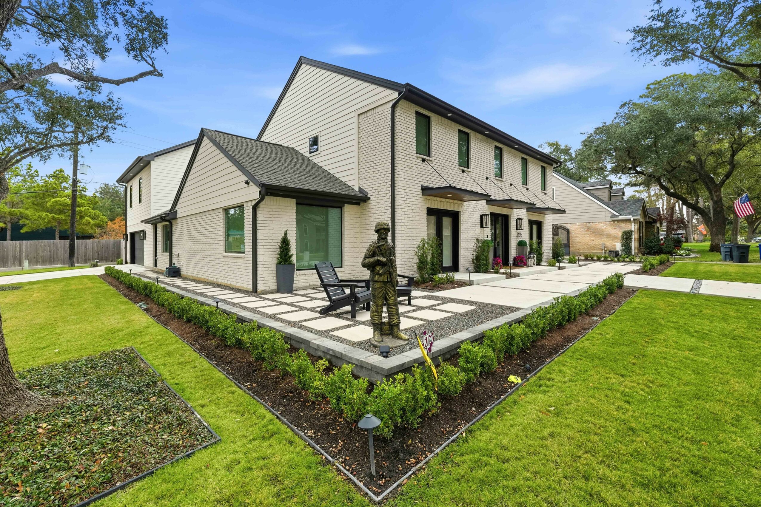 Modern two-story building with a landscaped garden, statue, benches, and trees in a sunny outdoor setting.