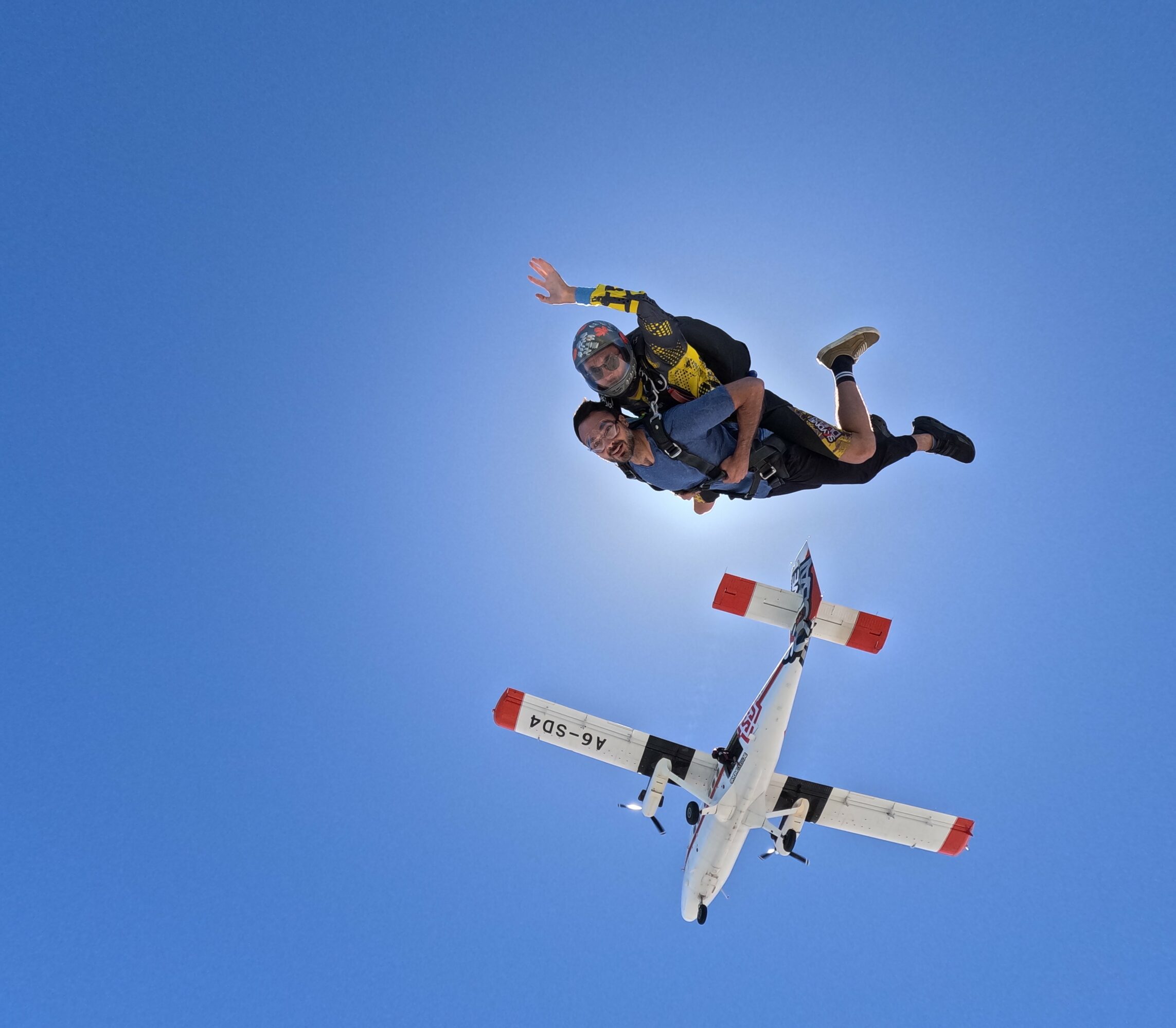 Two skydivers free-falling with a small airplane in clear blue sky.