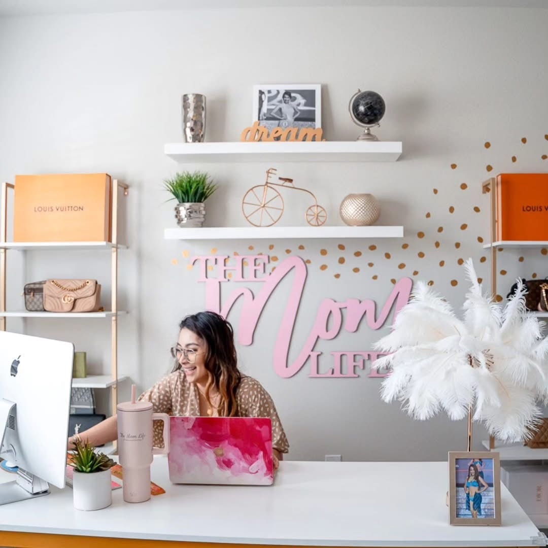 Woman sitting at desk with laptop, surrounded by decorative items and a large white feather arrangement.