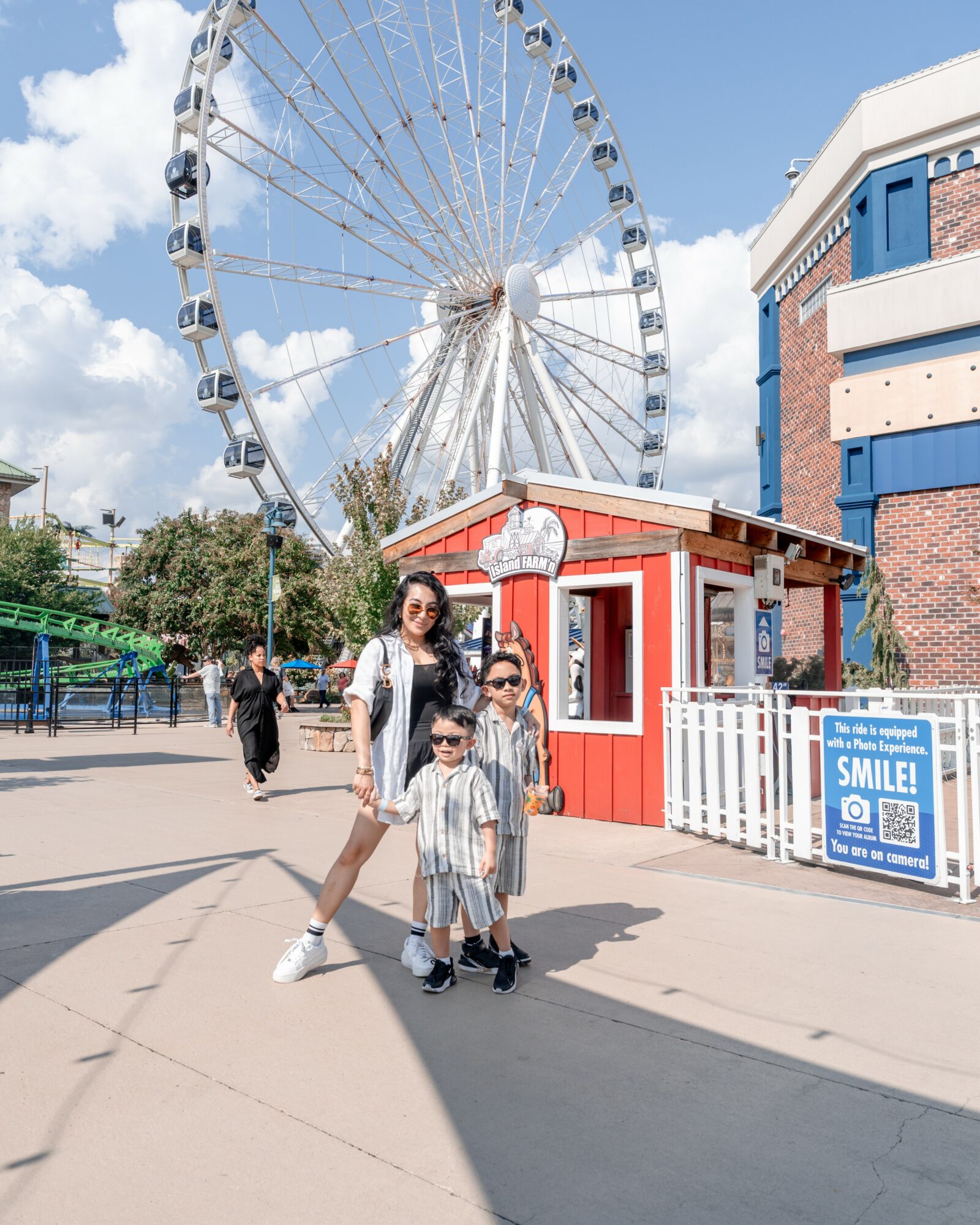 Family of three standing in front of a Ferris wheel at an amusement park, smiling and posing for the photo.