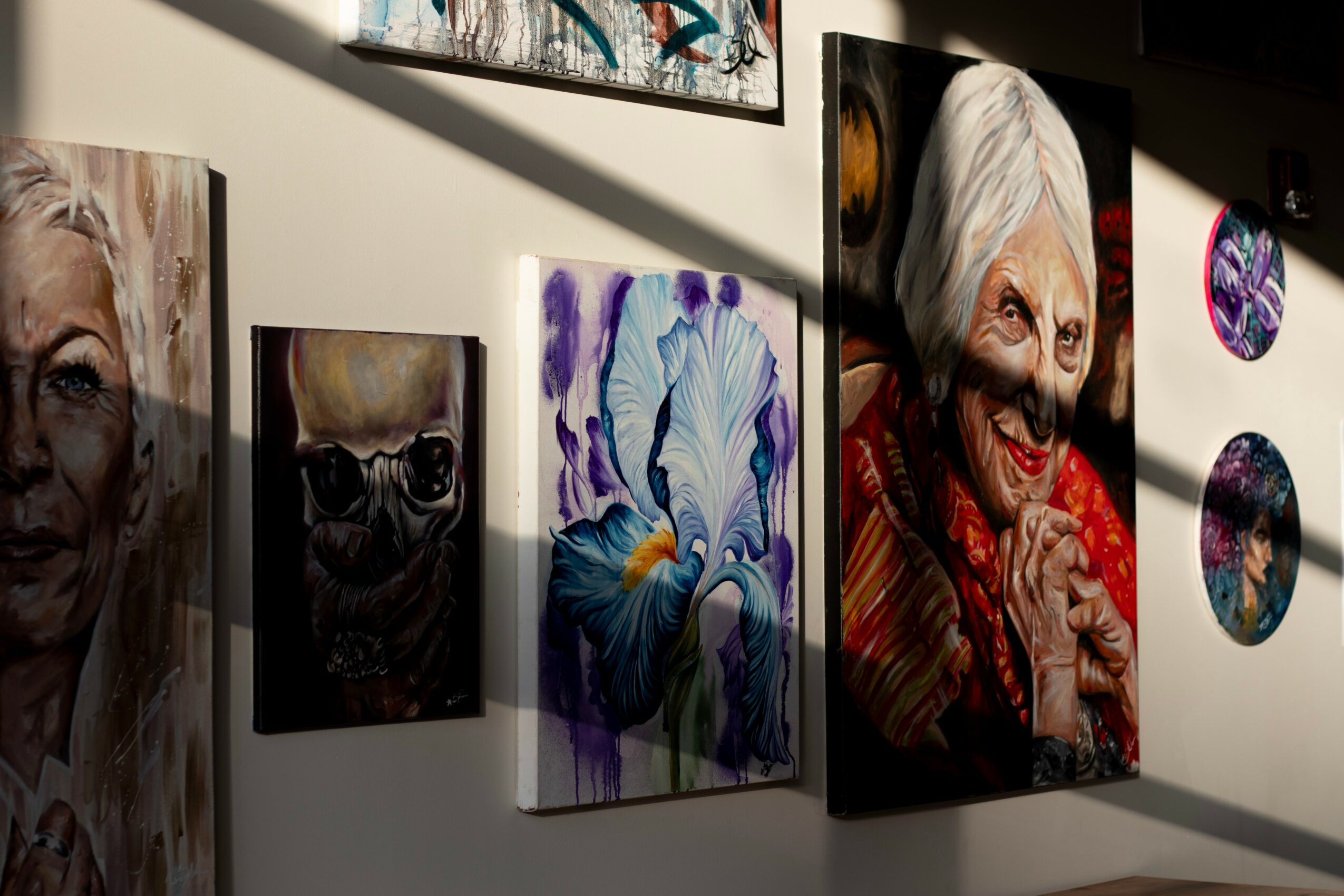 Gallery wall with colorful portraits and abstract paintings, including a smiling elderly woman and a person with glasses.