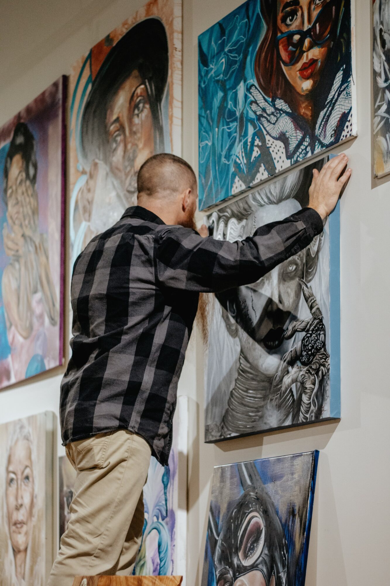 Person hanging a colorful portrait on a wall with other artwork displayed nearby.